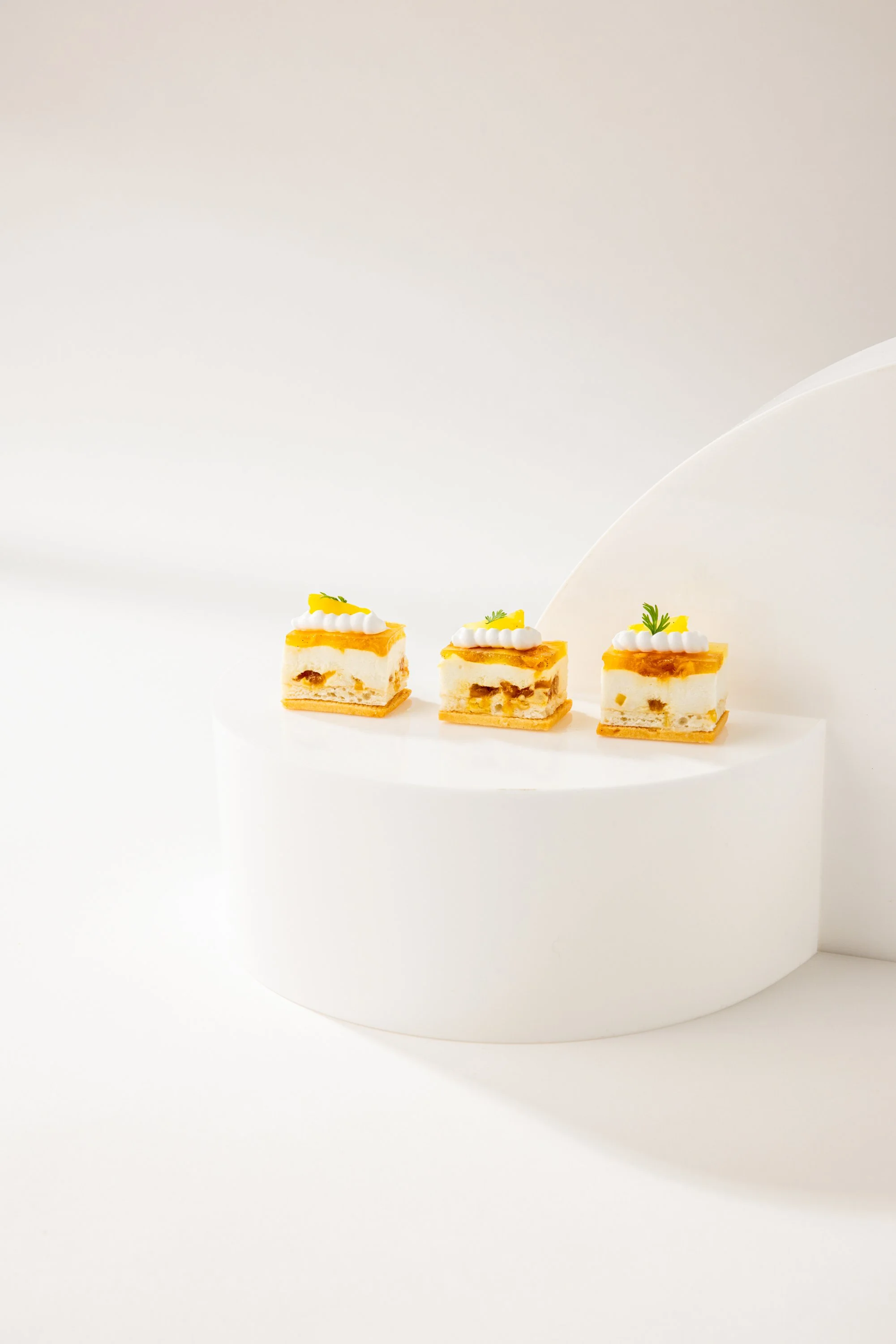 Three small, decorated dessert cakes on a white circular platform against a minimalist white background.