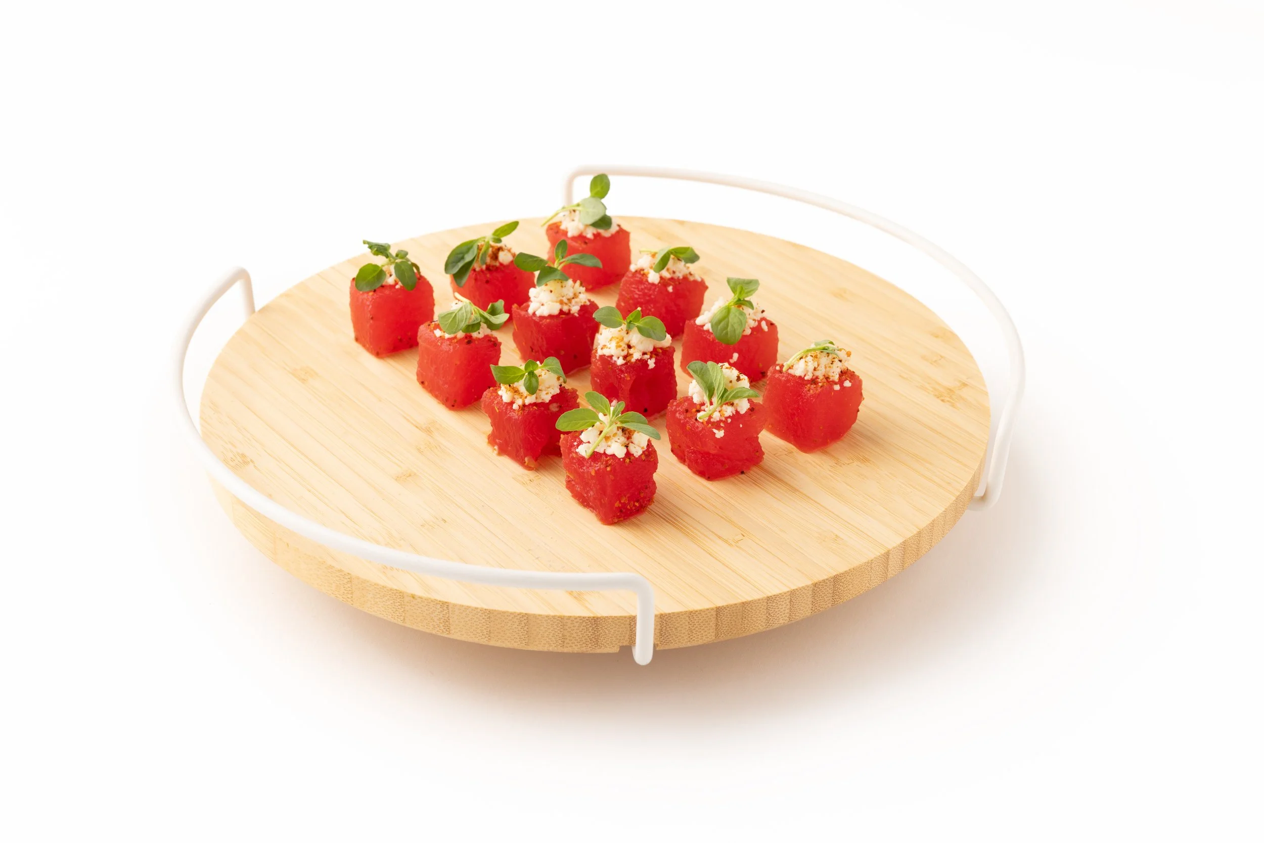 Small red watermelon cubes garnished with herbs and white cheese on a wooden serving board.