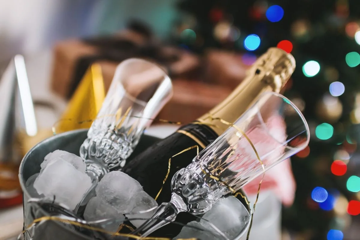 A bottle of champaign in an ice bucket with some glasses around it
