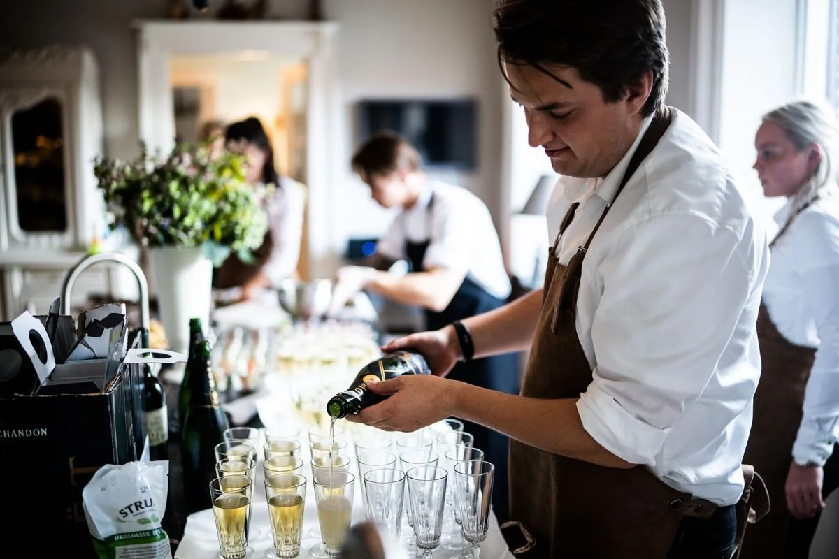 A server pouring champaign into a bunch of glasses for an event
