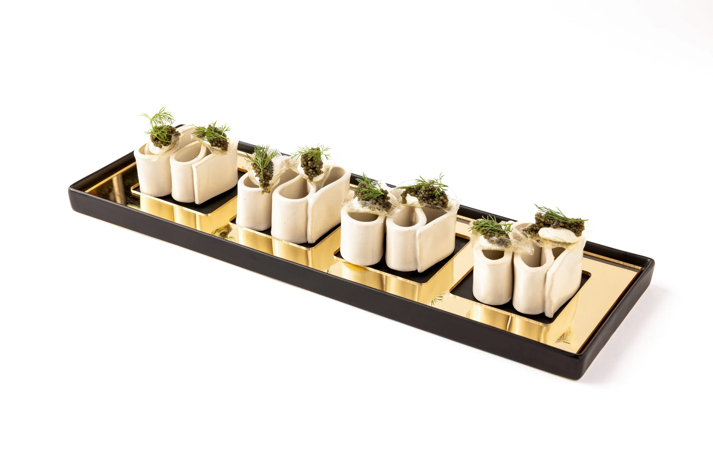 Elegant appetizer platter with white ceramic containers filled with caviar, garnished with herbs, on a black and gold tray.
