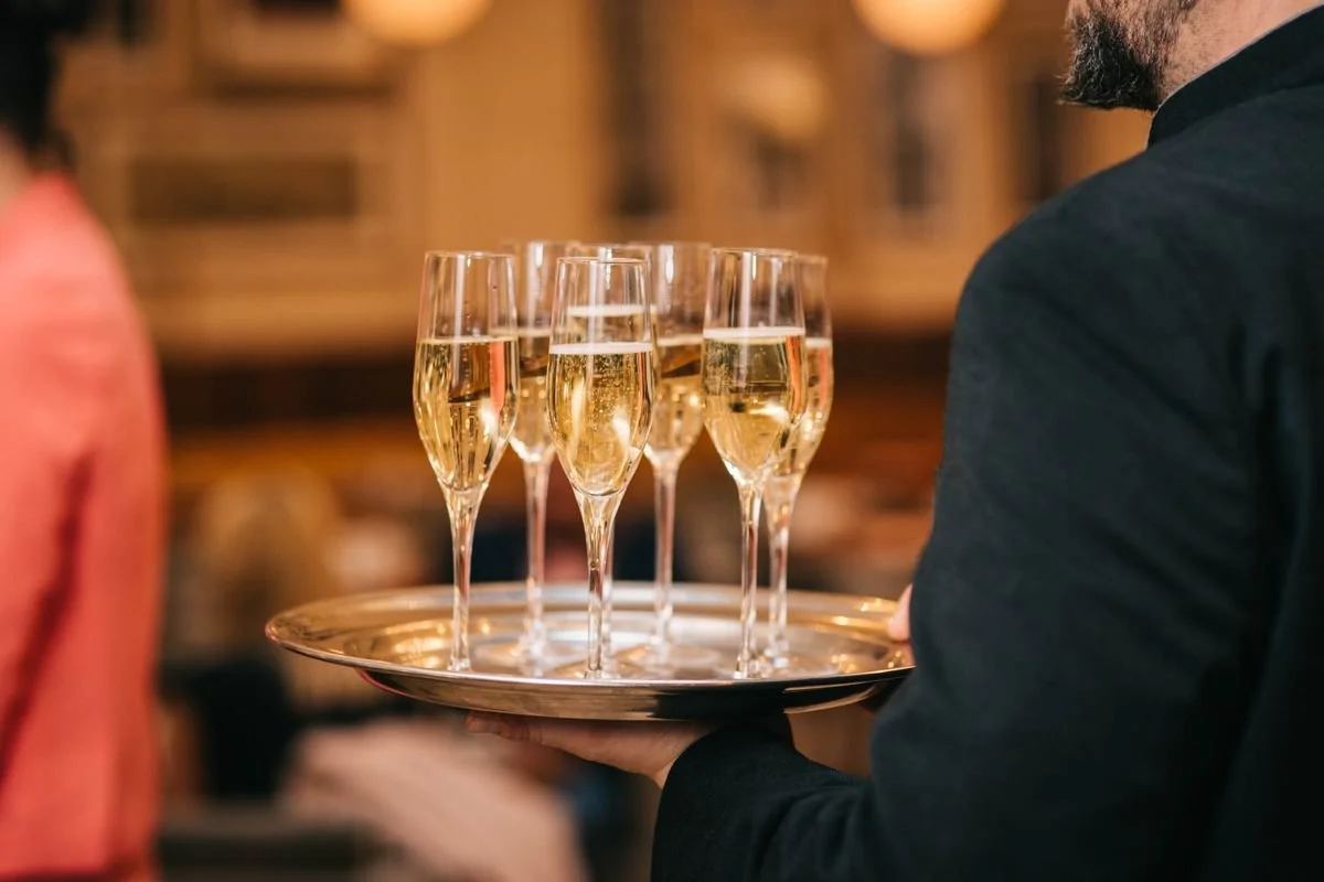 A bunch of champaign on a platter being moved by a waiter