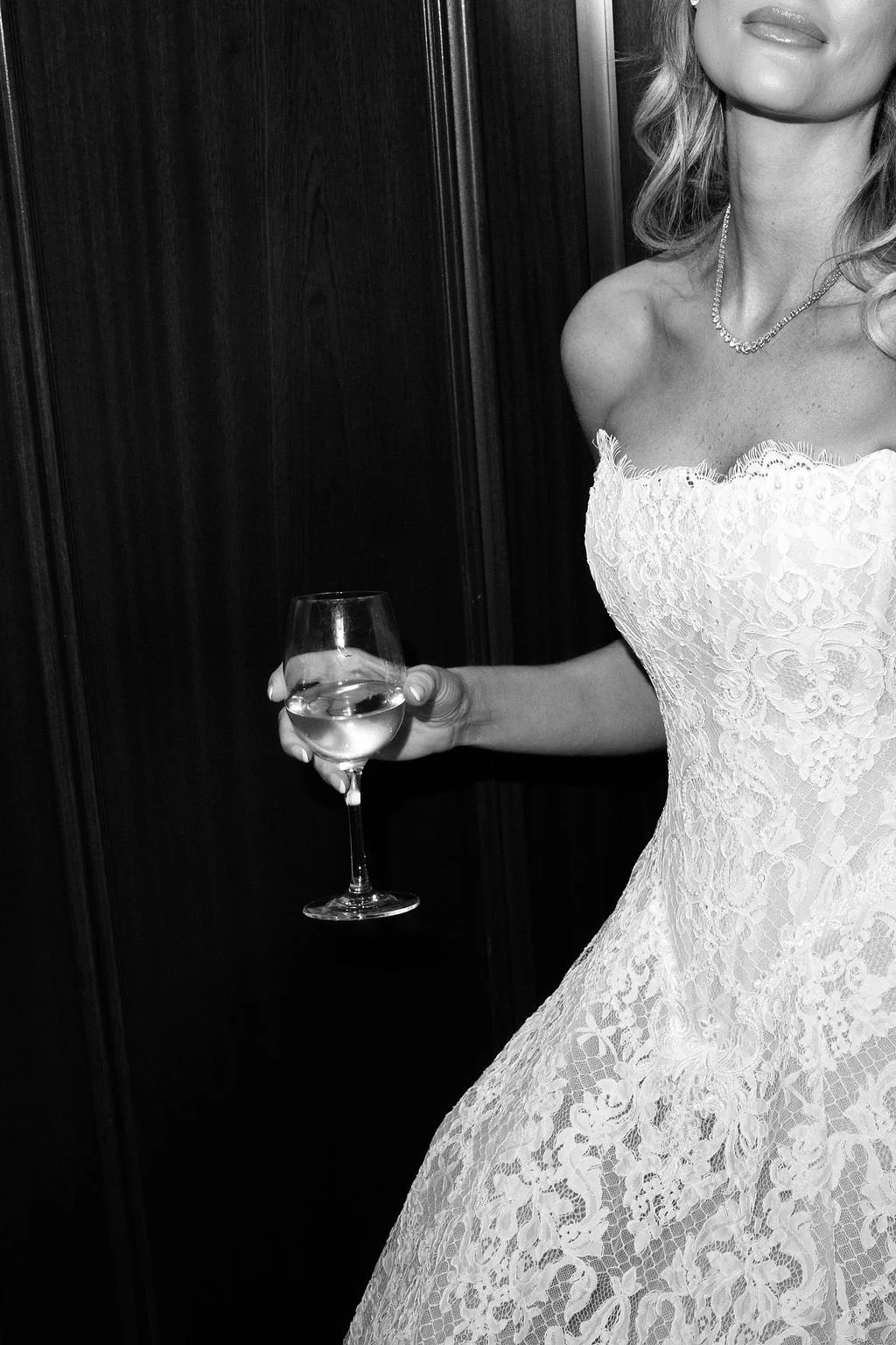 A woman in a strapless lace dress holding a glass of white wine.