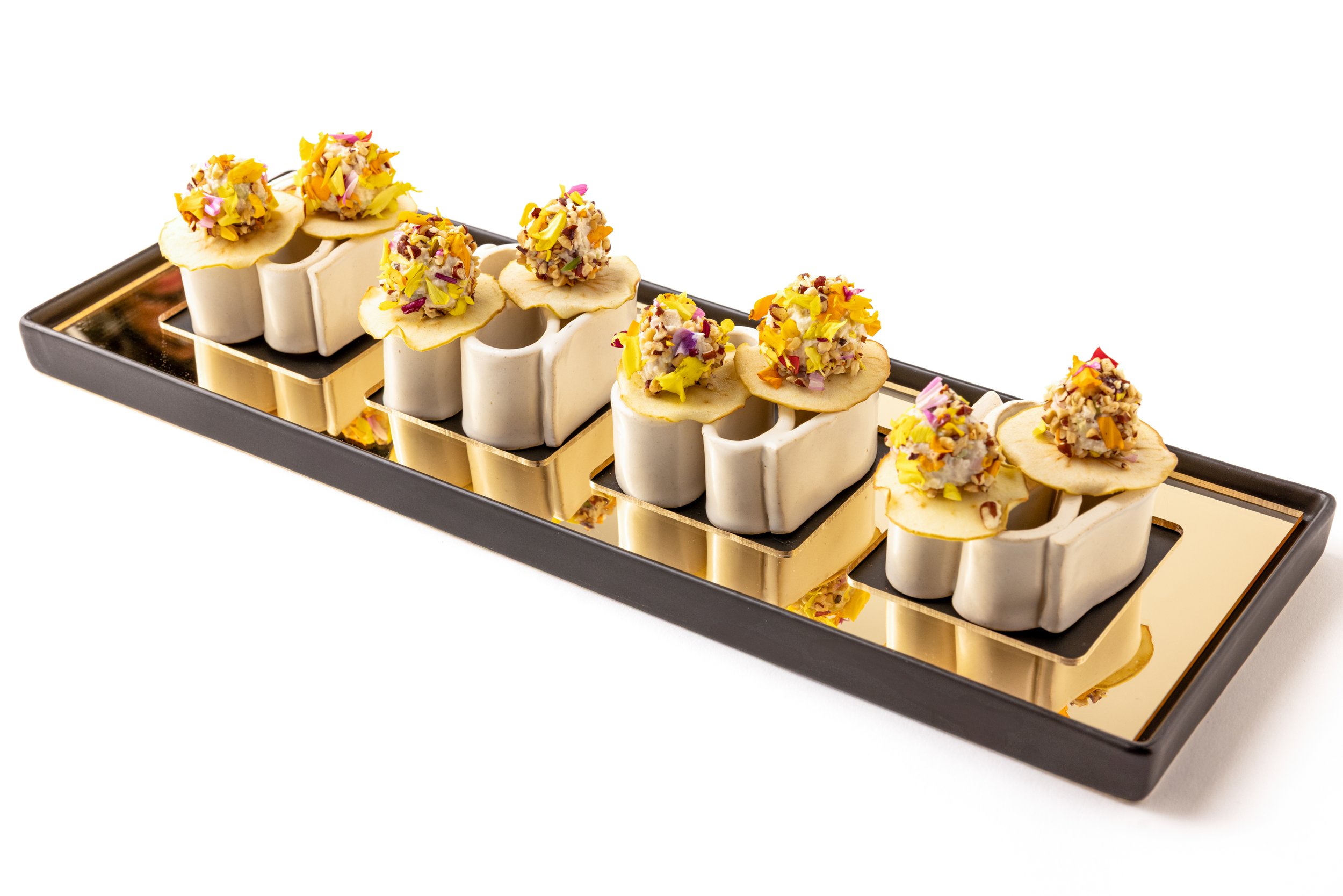 Presentation of colorful mini desserts topped with chopped nuts on a black and gold tray.