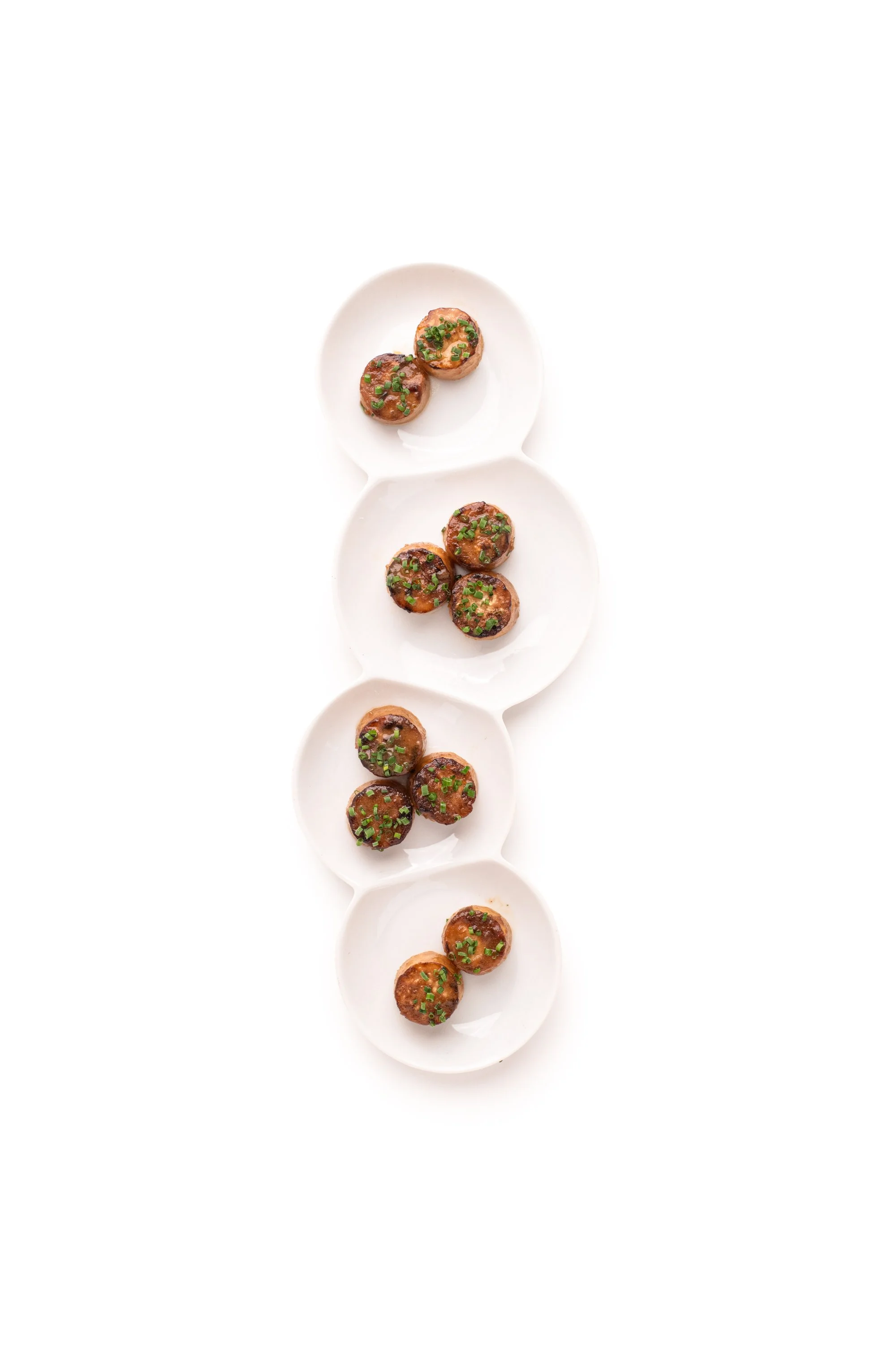 Multiple small meatballs garnished with chopped green herbs on white ceramic dishes.