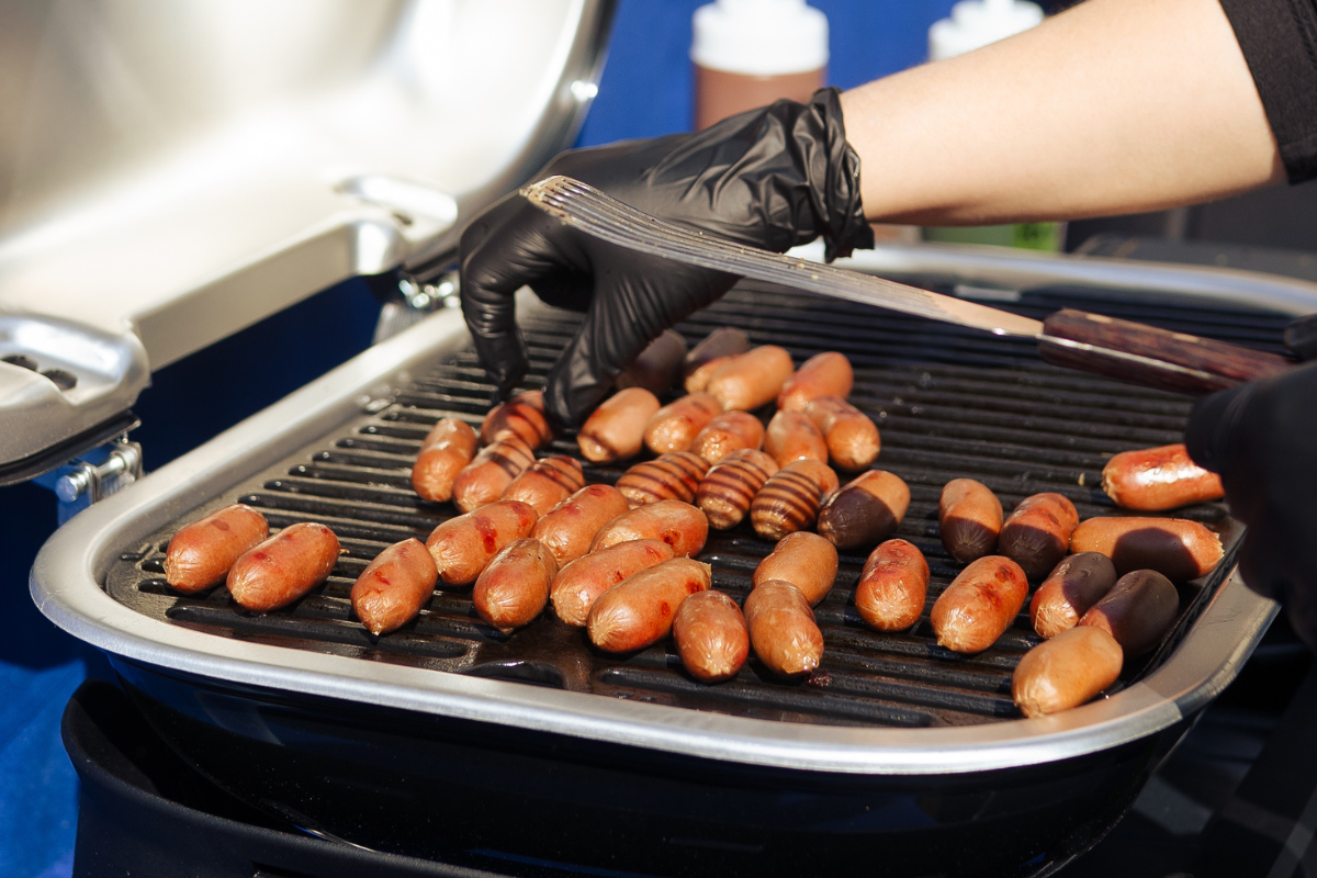 A bunch of little sausages cooking on a small grill