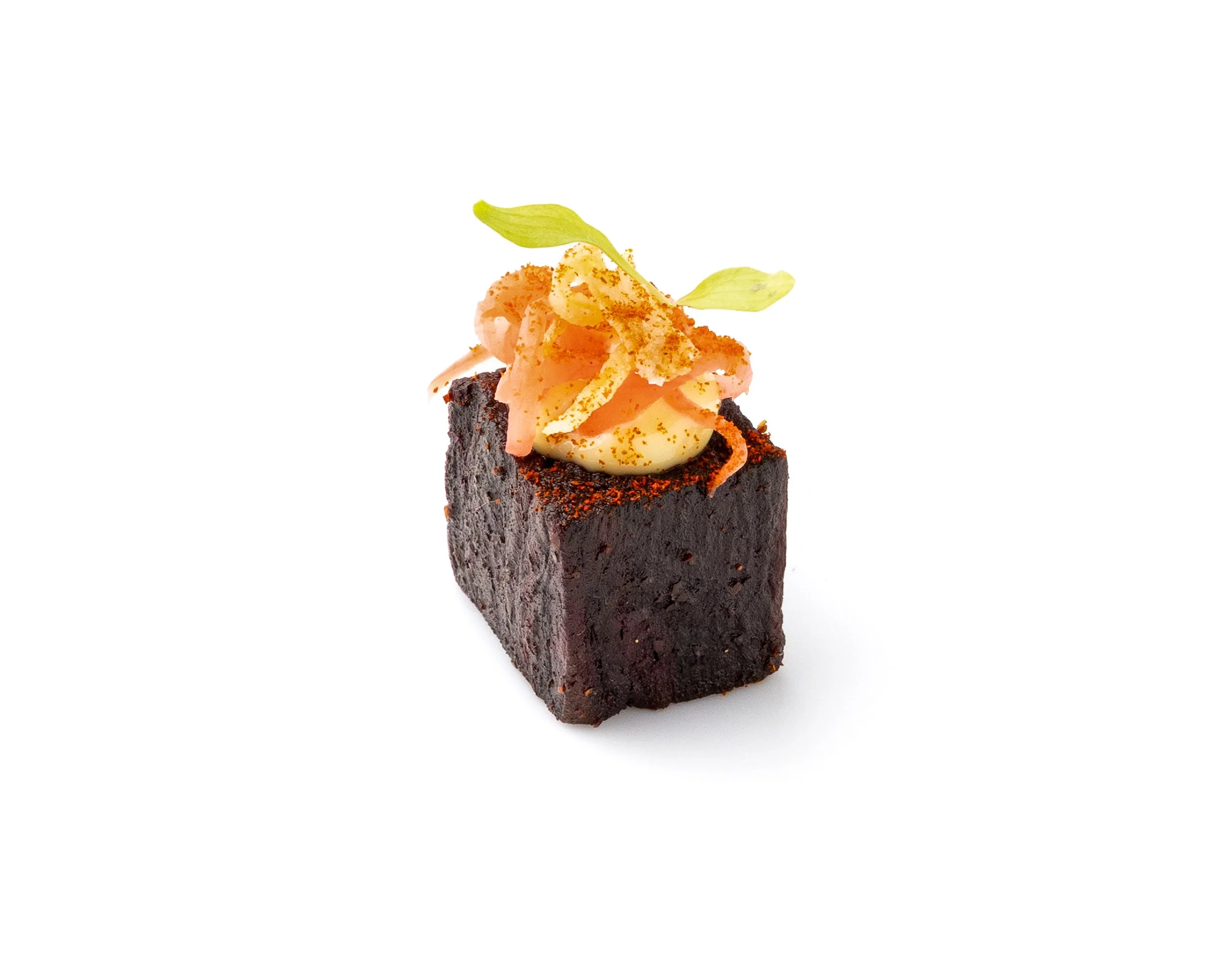 A piece of chocolate cake topped with a swirl of cream, orange zest, and small green leaves on a white background.
