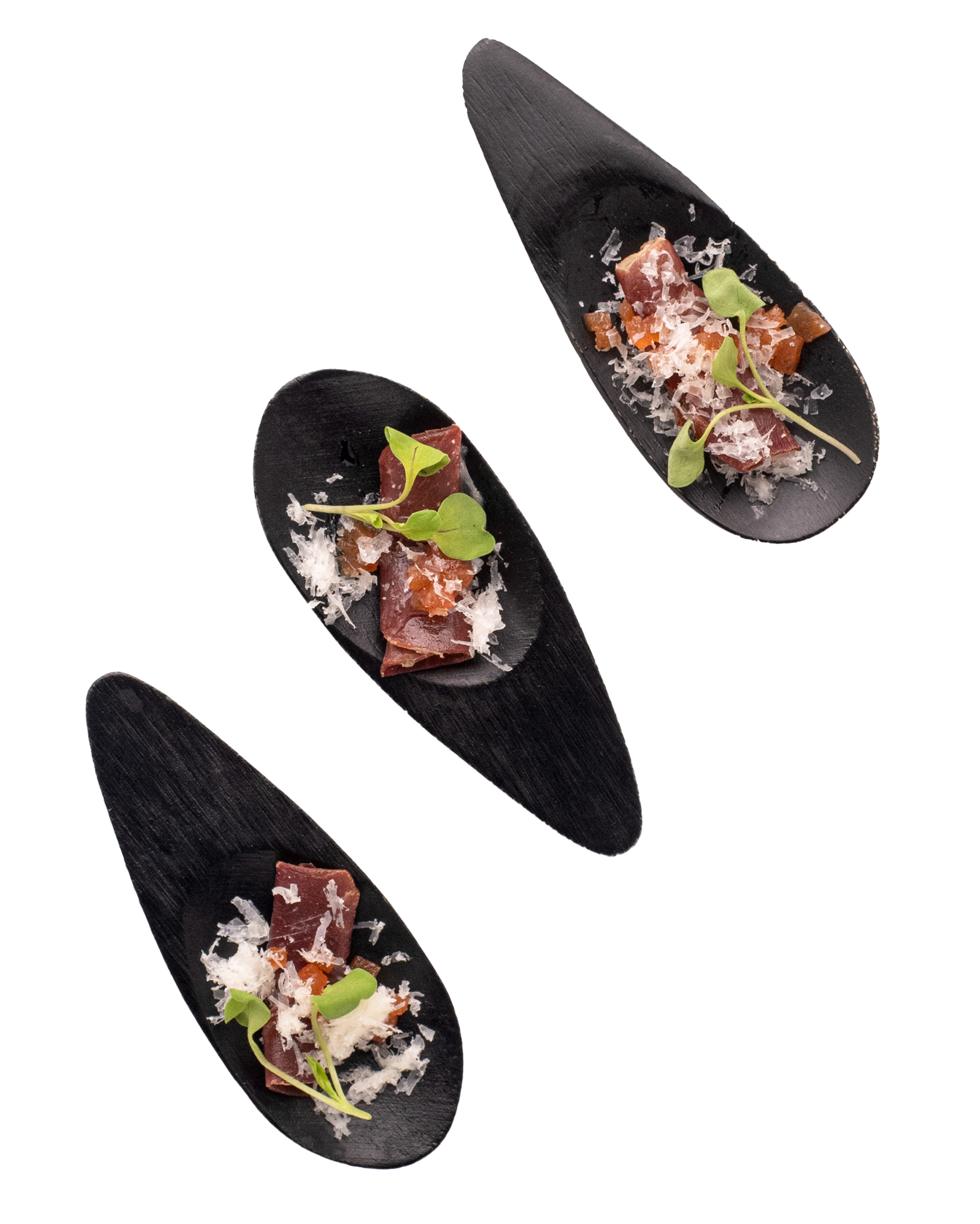 Three black spoons containing pieces of raw fish, grated cheese, small green microgreens, and orange bits, arranged diagonally.