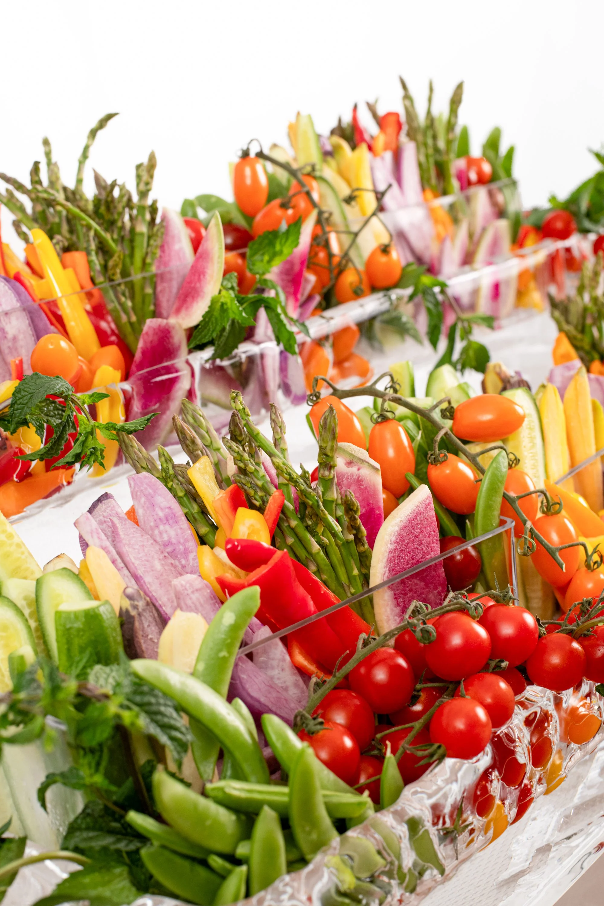 Assorted fresh vegetables including cherry tomatoes, asparagus, watermelon, bell peppers, and cucumbers arranged in a decorative display.