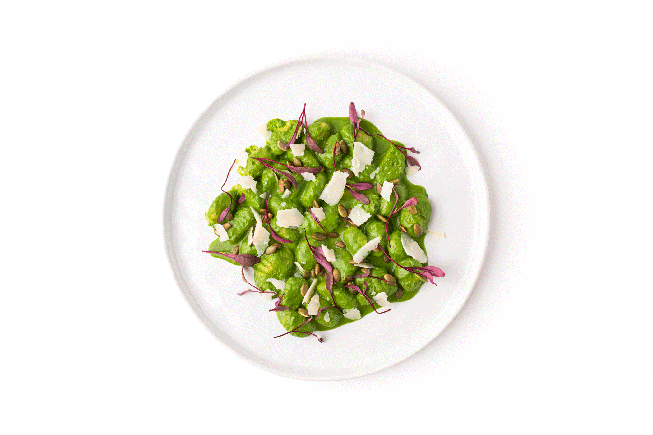 A white plate of green gnocchi garnished with cheese shavings, sunflower seeds, and microgreens.