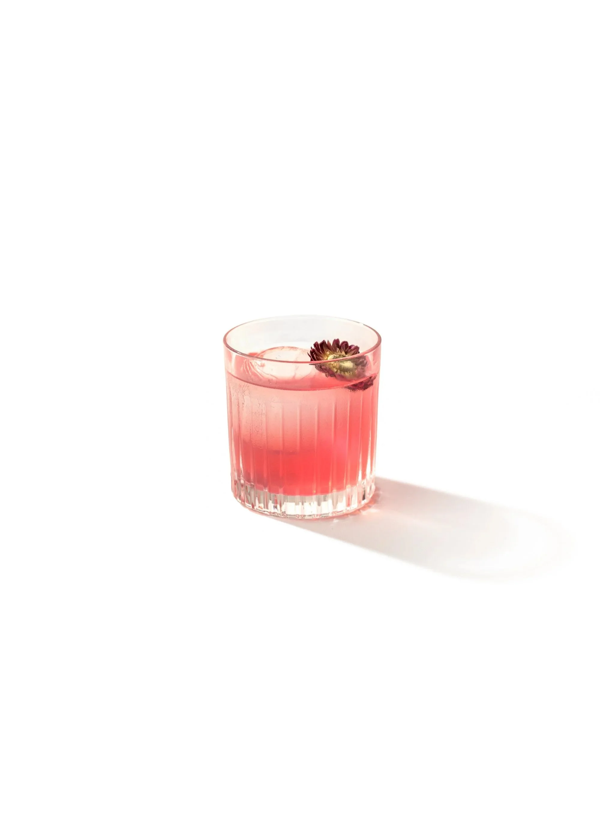 A pink beverage in a clear glass with a flower garnish on white background.