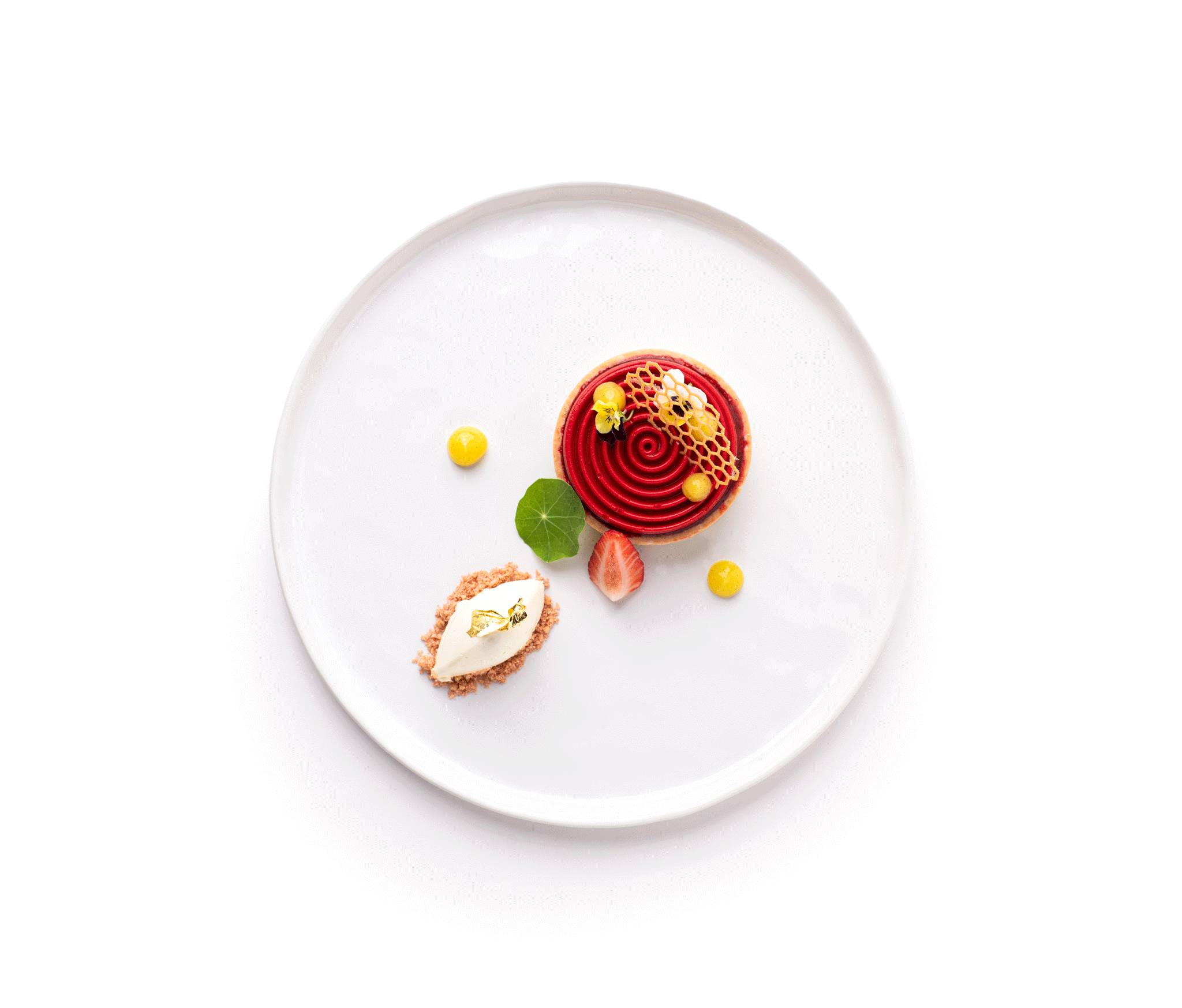 A modern dessert on a white plate featuring a round red spiral mousse decorated with a honeycomb and small edible flowers, accompanied by a green leaf, a sliced strawberry, and a dollop of white cream garnished with a gold leaf.