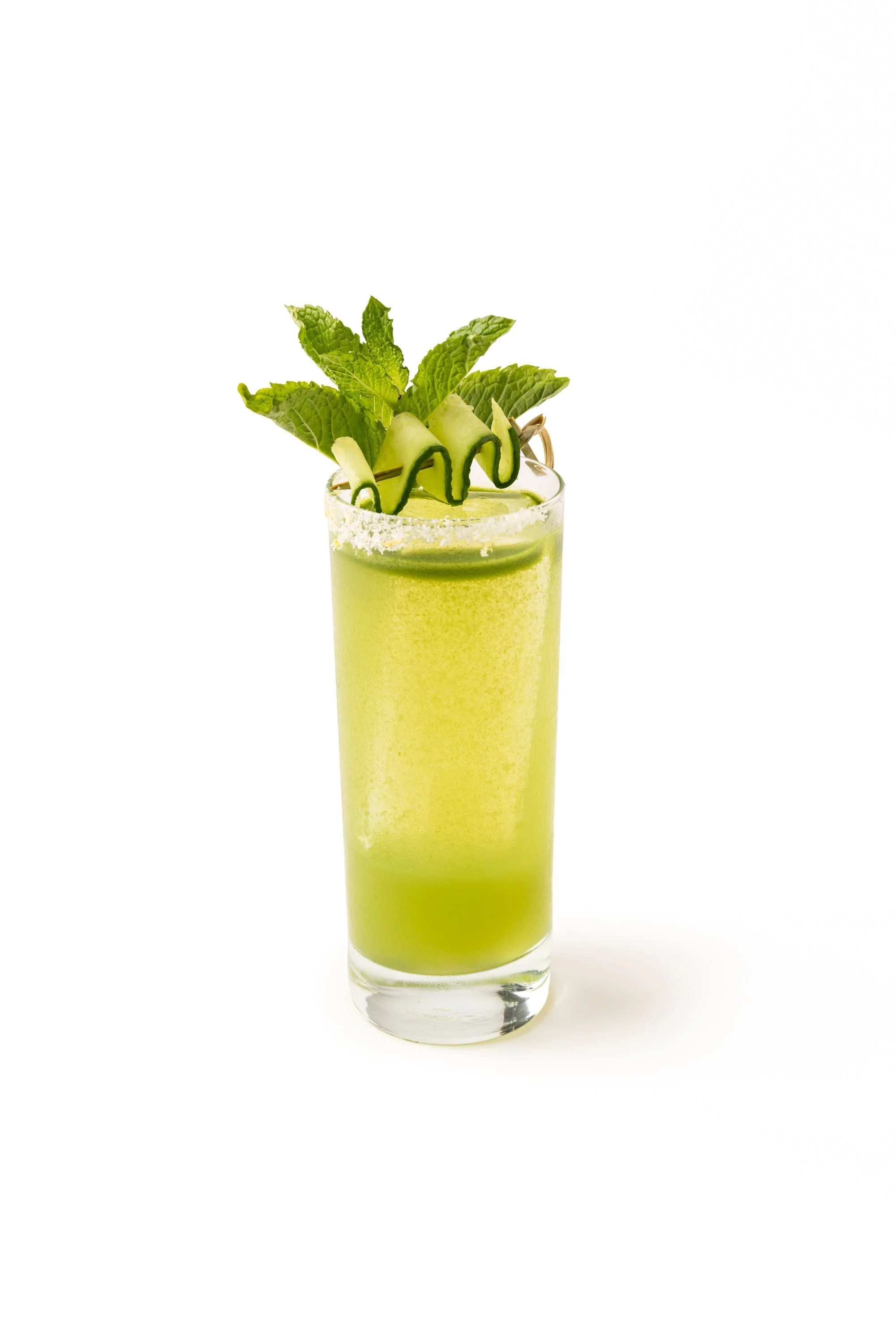 A tall glass of green smoothie garnished with mint leaves, cucumber slices, and a decorative cucumber spiral on top, with a salted rim.