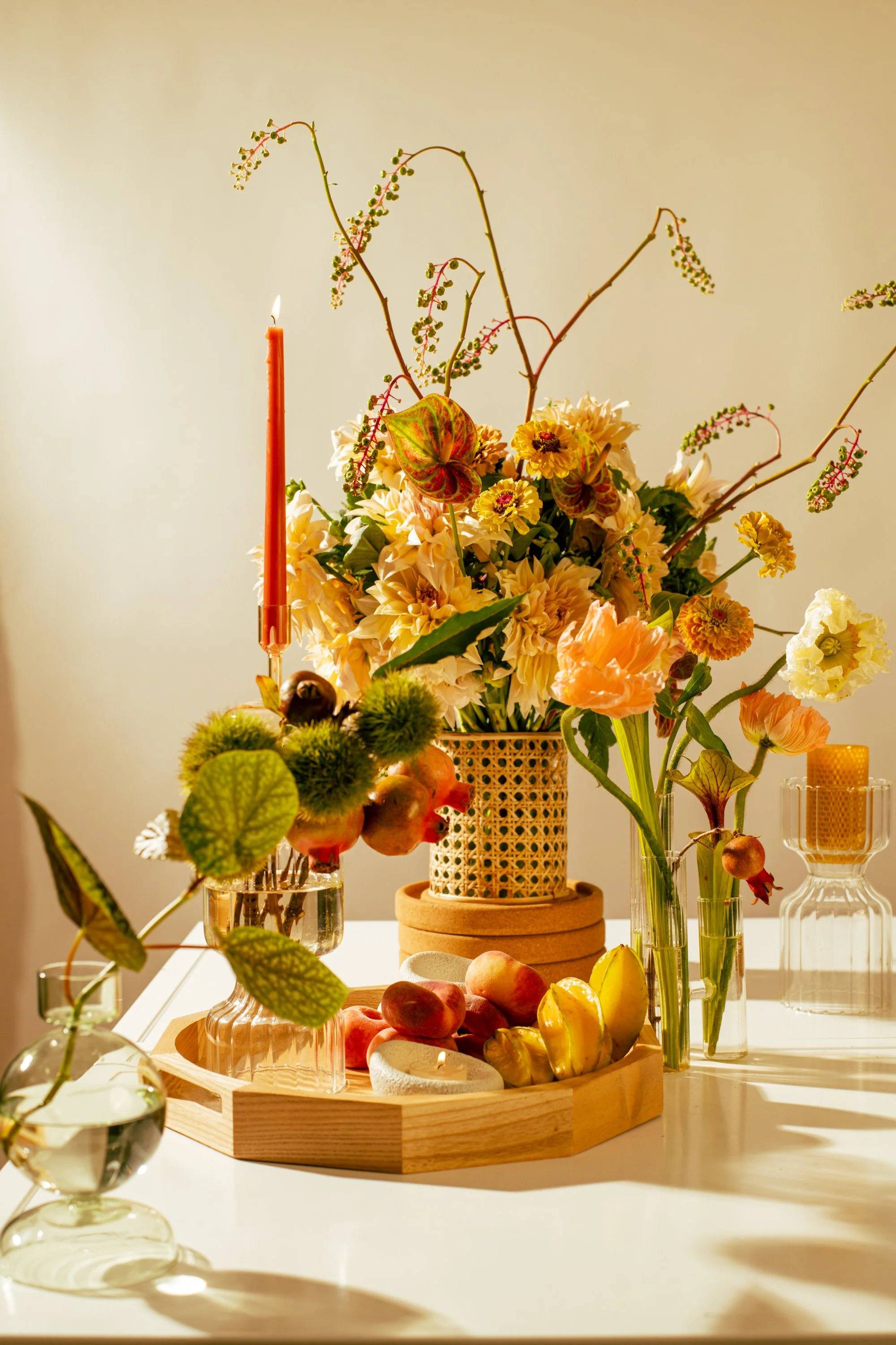 A table decorated with a floral arrangement, a lit candle, and various vases and decorative items illuminated by warm sunlight.