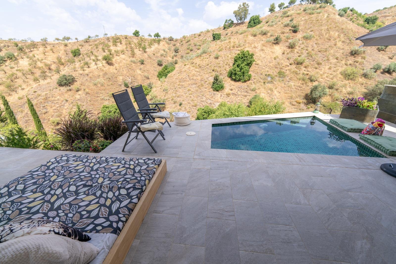 Privater Pool auf einer Terrasse mit Blick auf eine hügelige, trockene Landschaft mit vereinzelt grünen Büschen und Bäumen.