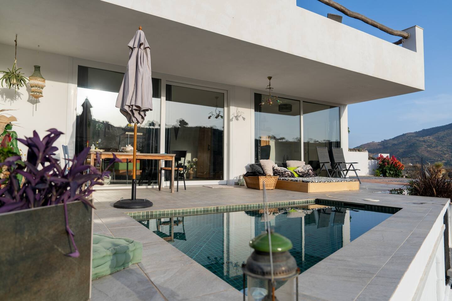 Moderne Hausterrasse mit Pool, bequemen Liegen, Sonnenschirm, und Blick auf Berge