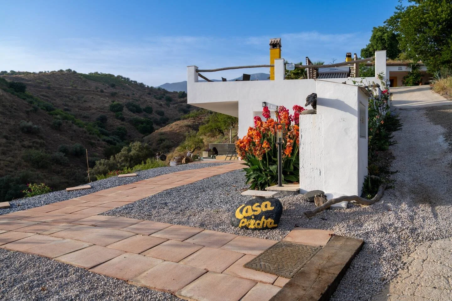 Häuschen mit weißer Fassade, Blumen und terrassierter Außenbereich in bergiger Landschaft