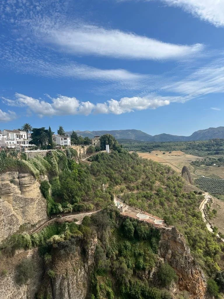 Blick auf eine malerische Landschaft mit weißen Häusern auf einer Klippe, umliegende grüne Hügel und einen blauen Himmel mit Wolken.