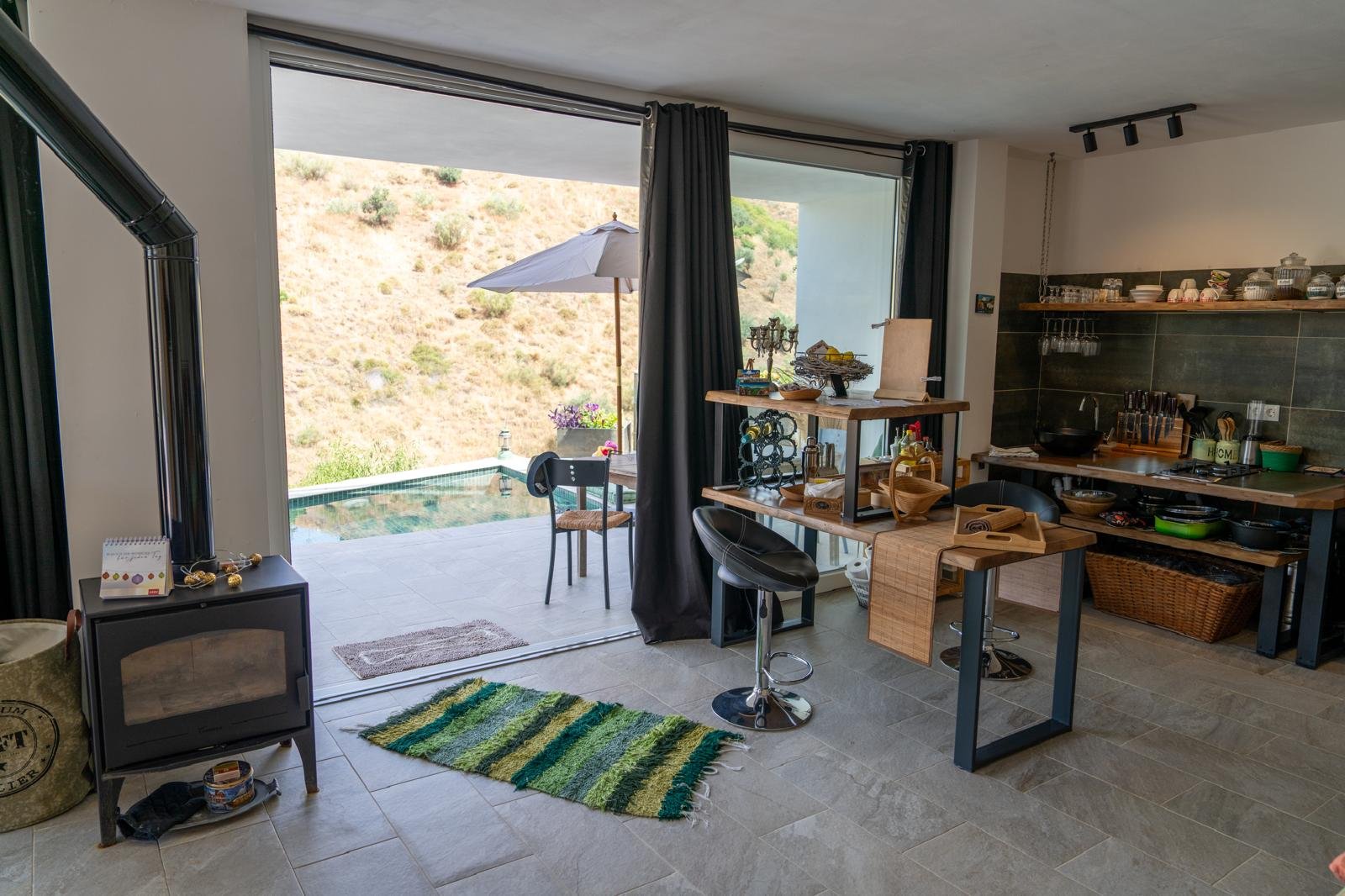 Moderner Küchenbereich mit Blick auf eine Terrasse mit Sonnenschirm und Pool, offen gestaltet mit Holzmöbeln, Küchenutensilien und dekorativen Gegenständen.