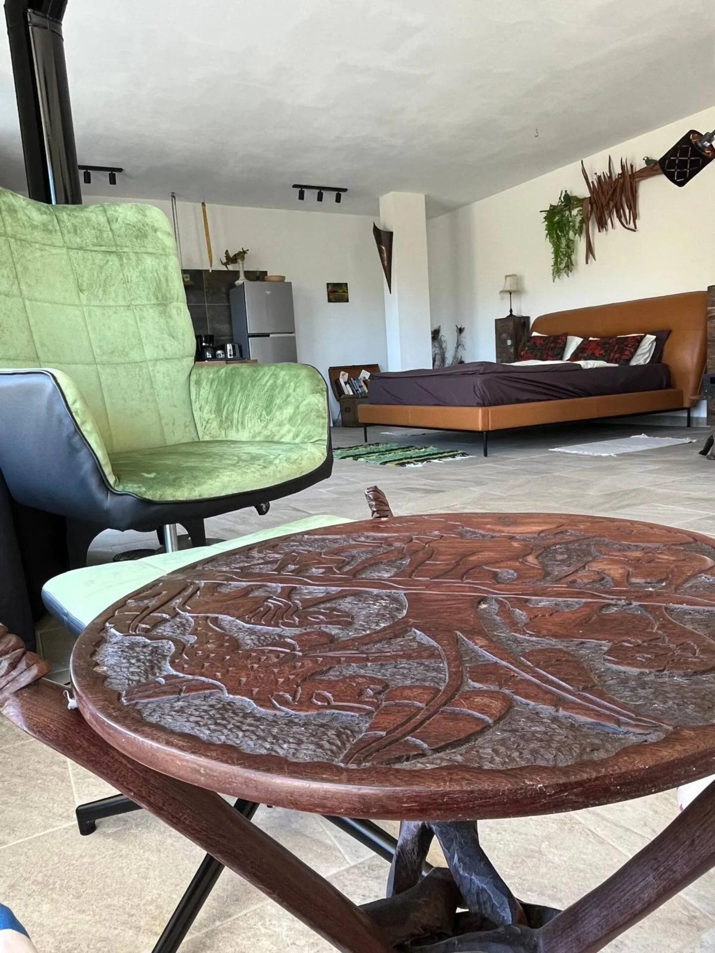 Innenraum eines Wohnzimmers mit grünem Sessel, braunem Bett und Holztisch im Vordergrund.