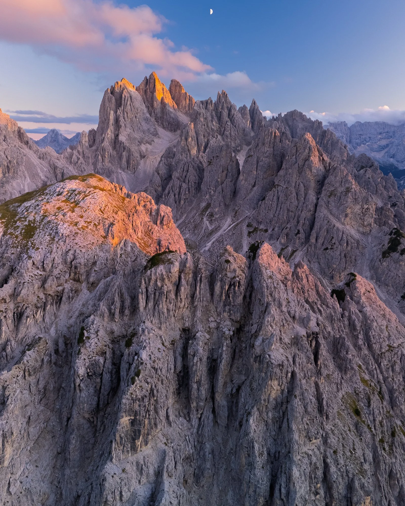 Mountain range during sunset with rocky peaks and a moon in the sky.