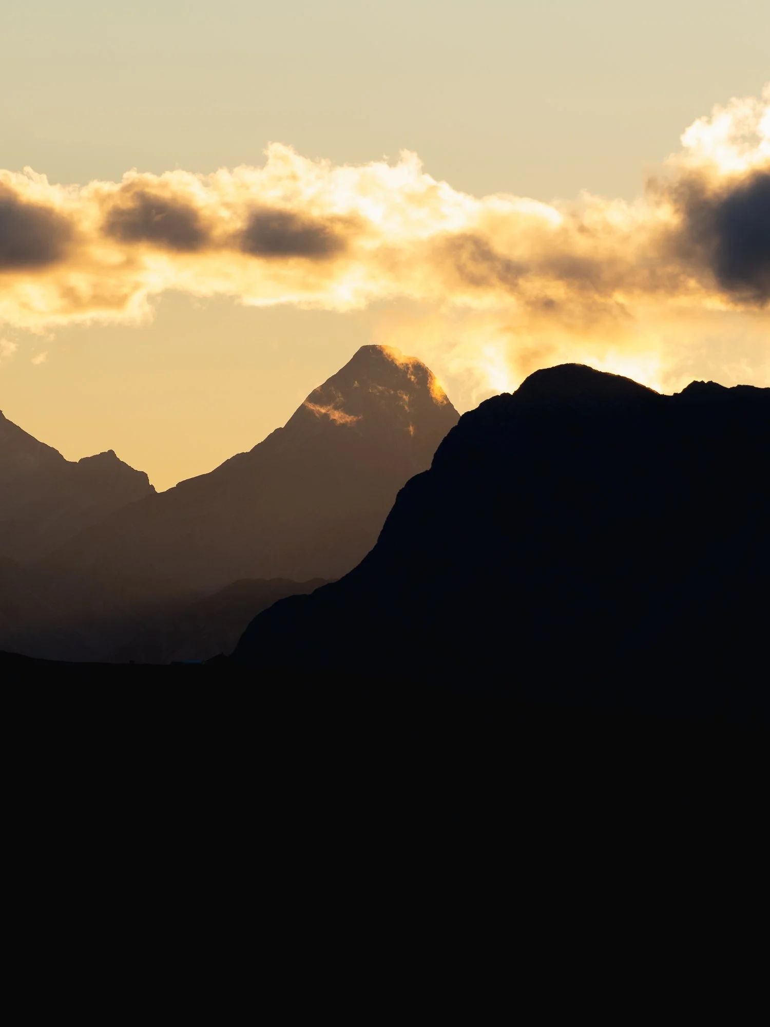 Mountain landscape during sunset with silhouetted mountains and clouds in the sky.