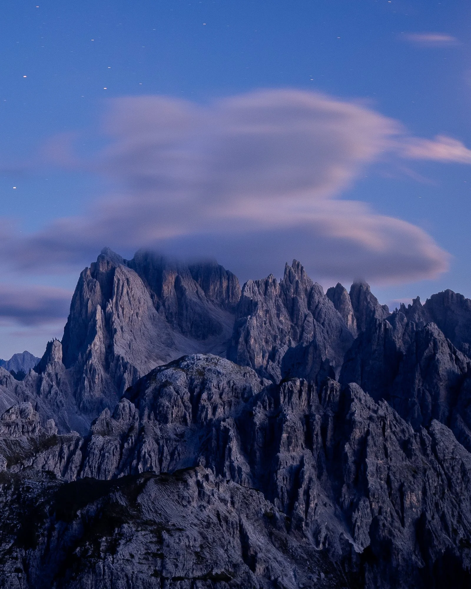 Mountain landscape during twilight with clouds and visible stars in the sky.