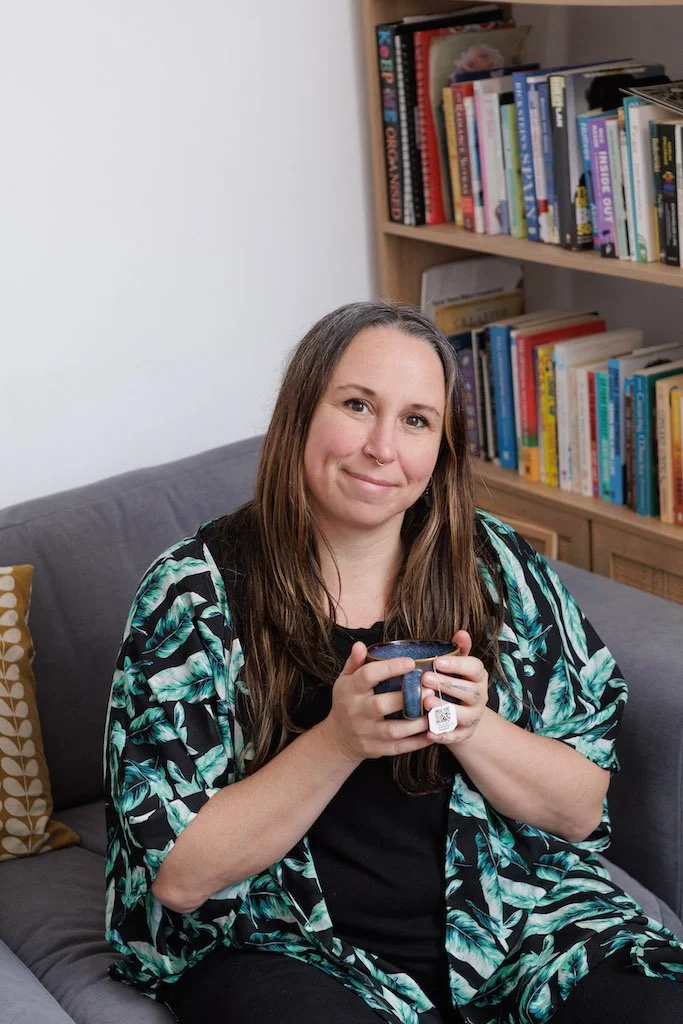 Portrait of a somatic rest and nervous system support practitioner sitting with a cup of tea, offering a calm and welcoming presence.