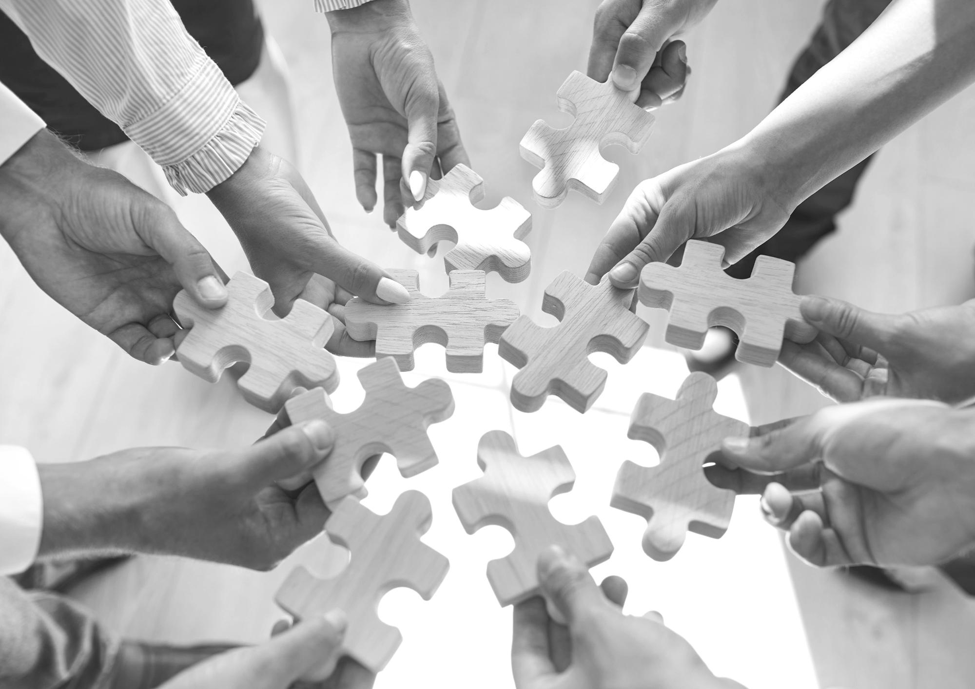 Mehrere Hände, die ein Holzpuzzle zusammenfügen.