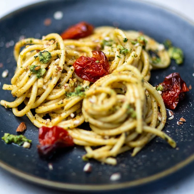 Plate of spaghetti with sun-dried tomatoes, chopped herbs, and grated cheese