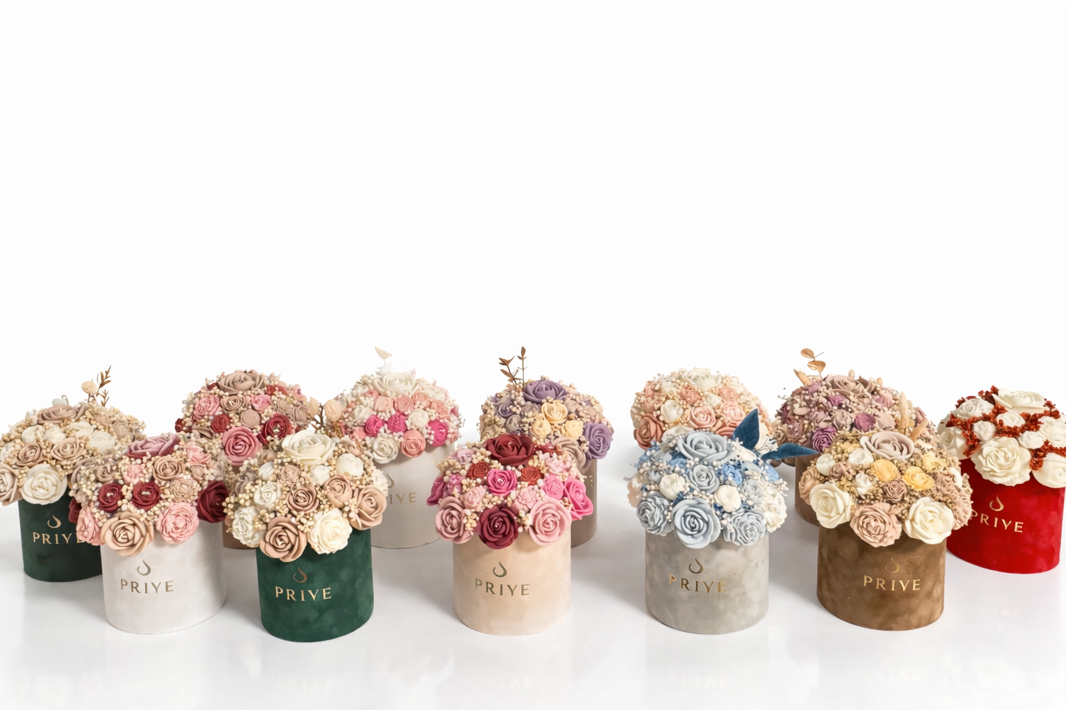 Multiple bouquets of pink, white, purple, and red flowers in colorful cylindrical boxes labeled 'PRIYE' on a white surface.
