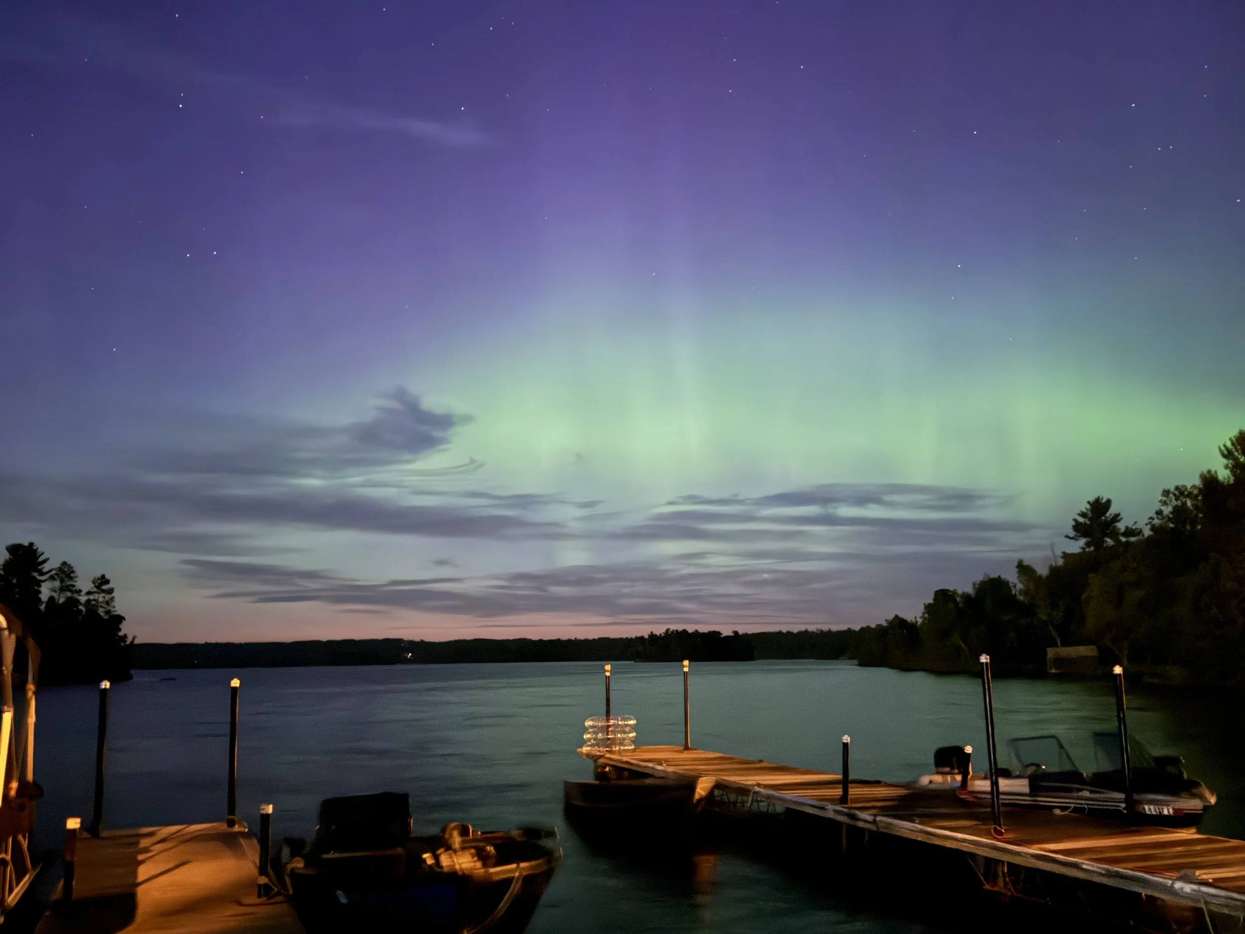 Northern lights over Shagawa lake with a dock and boats at dusk.