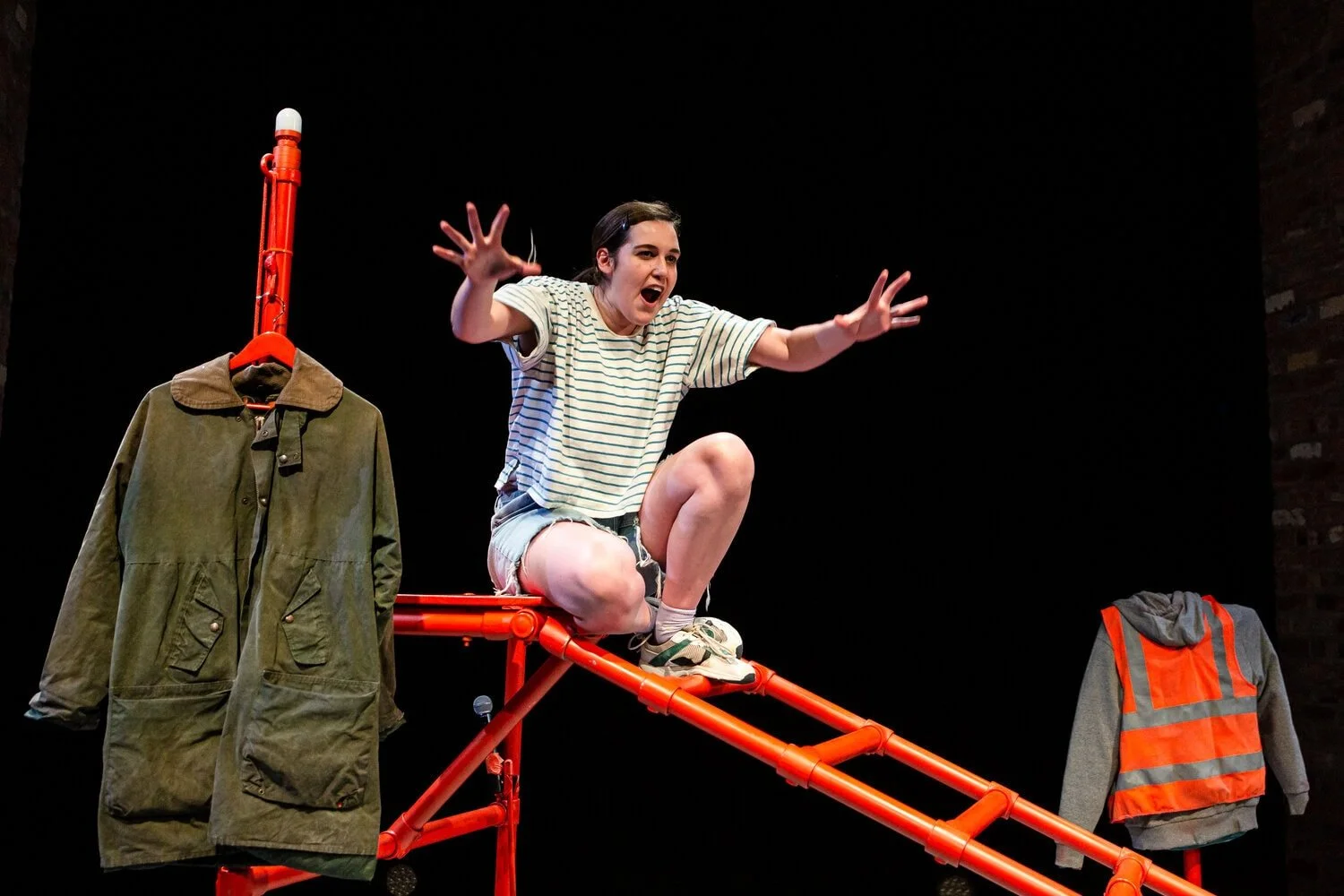 Safi sits on the orange frame with mouth open and arms and hands stretched out in front of her.