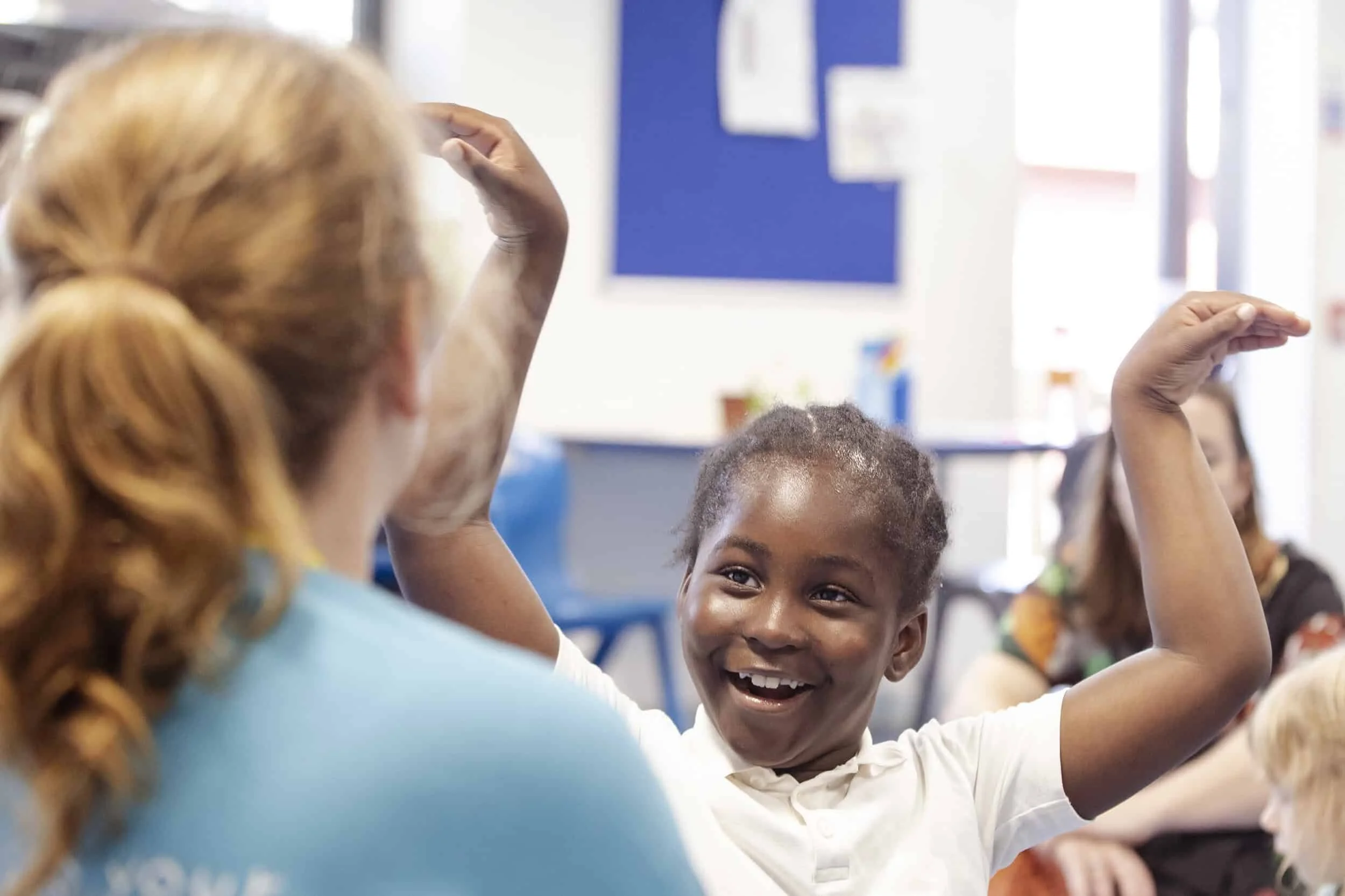 A pupil looks at a facilitator with their arms help up.