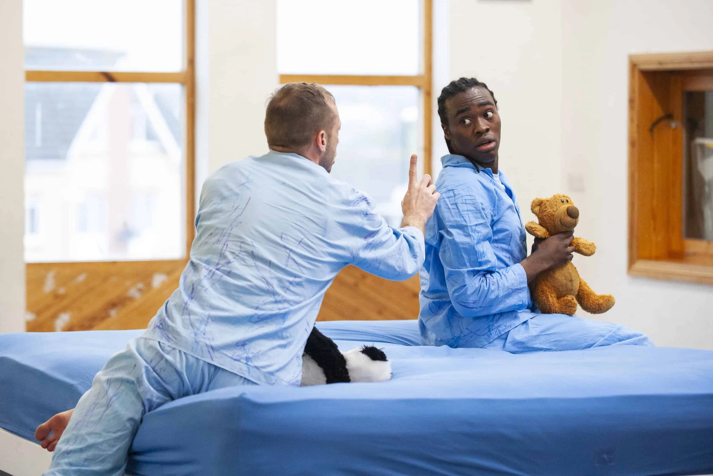 Wilkie and kel sit on a blue mattress both holding a teddy.