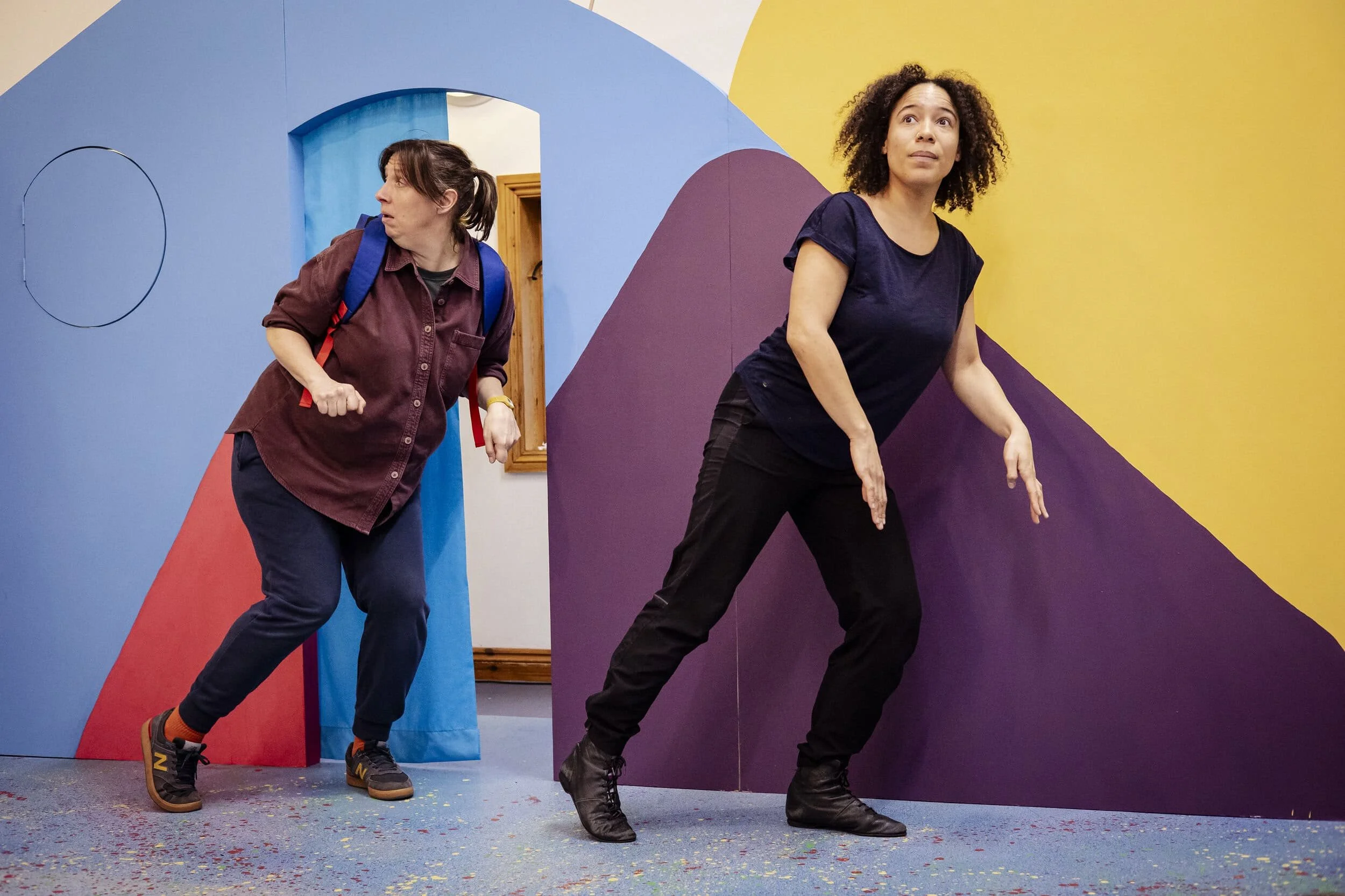Amy and Remi performing in The Forest Door - they are creeping across the stage with a colourful set behind them.