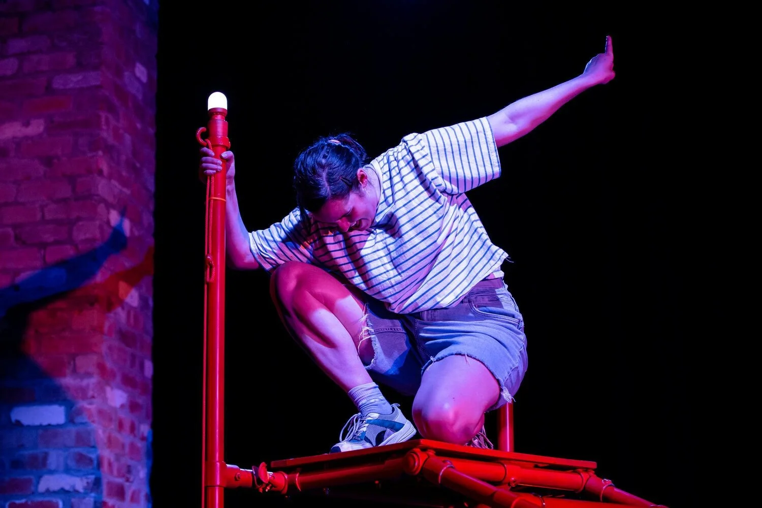 Safi kneels on the orange frame with one hand holding the frame and one arm stretched out above her with finger pointing towards the sky.