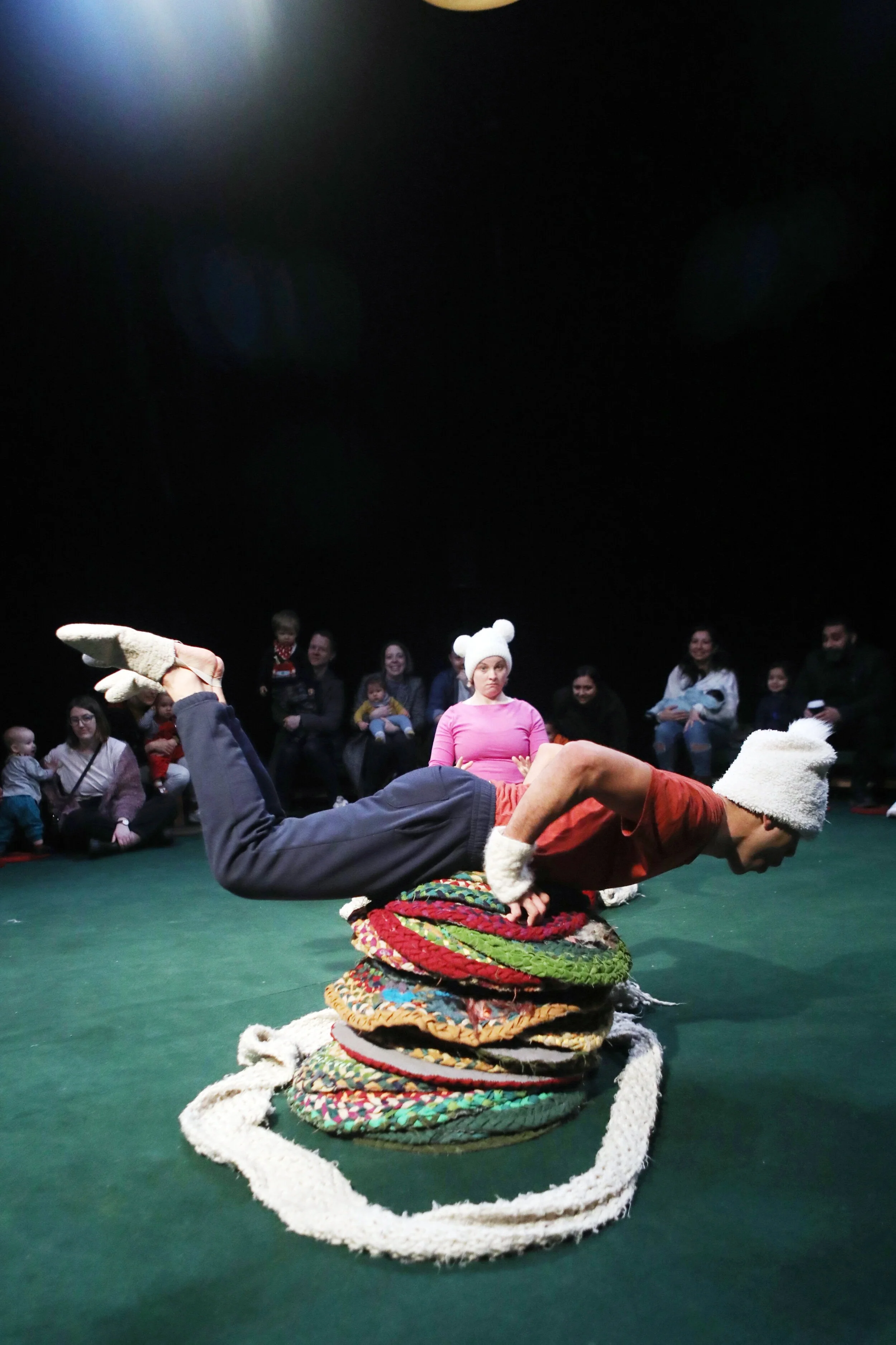 Sadie is lying horizontally over a pile of colourful circle mats while Ira looks on in the background.