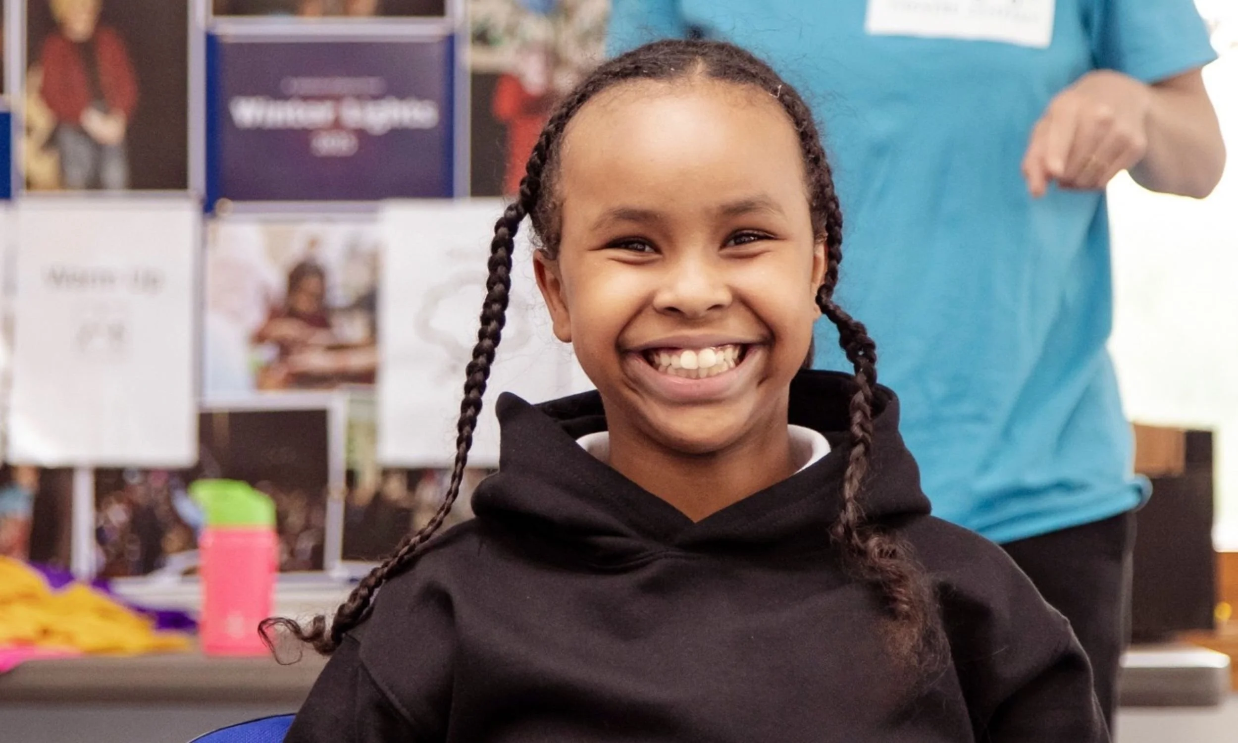 A member of Louder Than Words sits on a chair with a big smile on their face.
