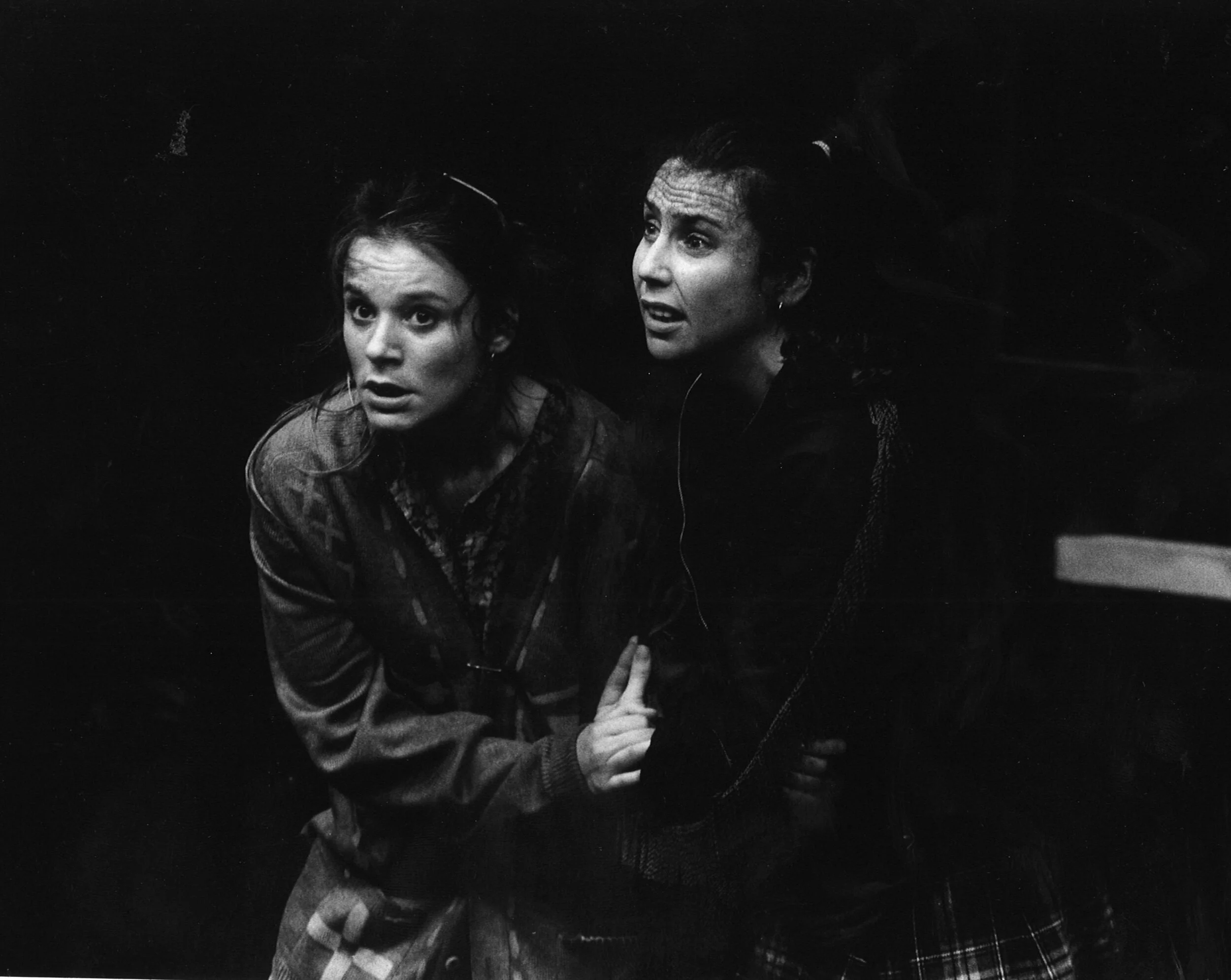 Two actors look up at something above them in a dark setting, one actor is pointing with her finger.
