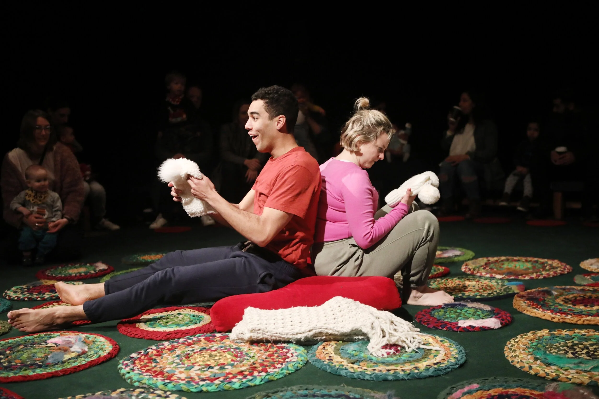 Sadie and Ira sit on a red cushion with their backs together and facing away from each other, surrounded by colourful circle mats.