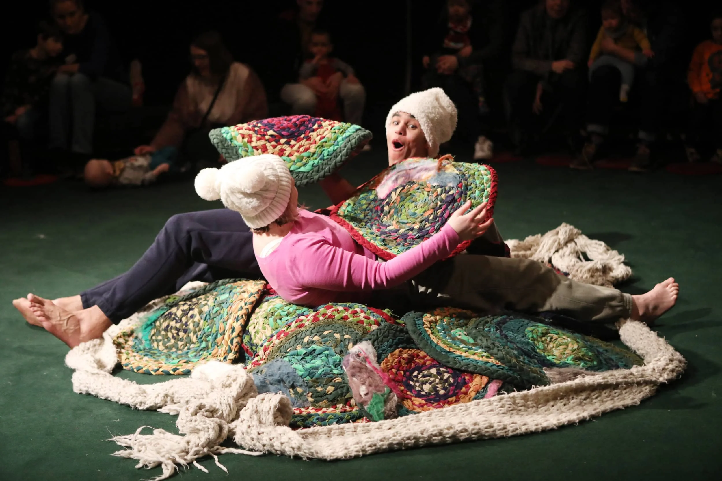 Ira and Sadie lie on a pile of colourful mats looking at eaech other.