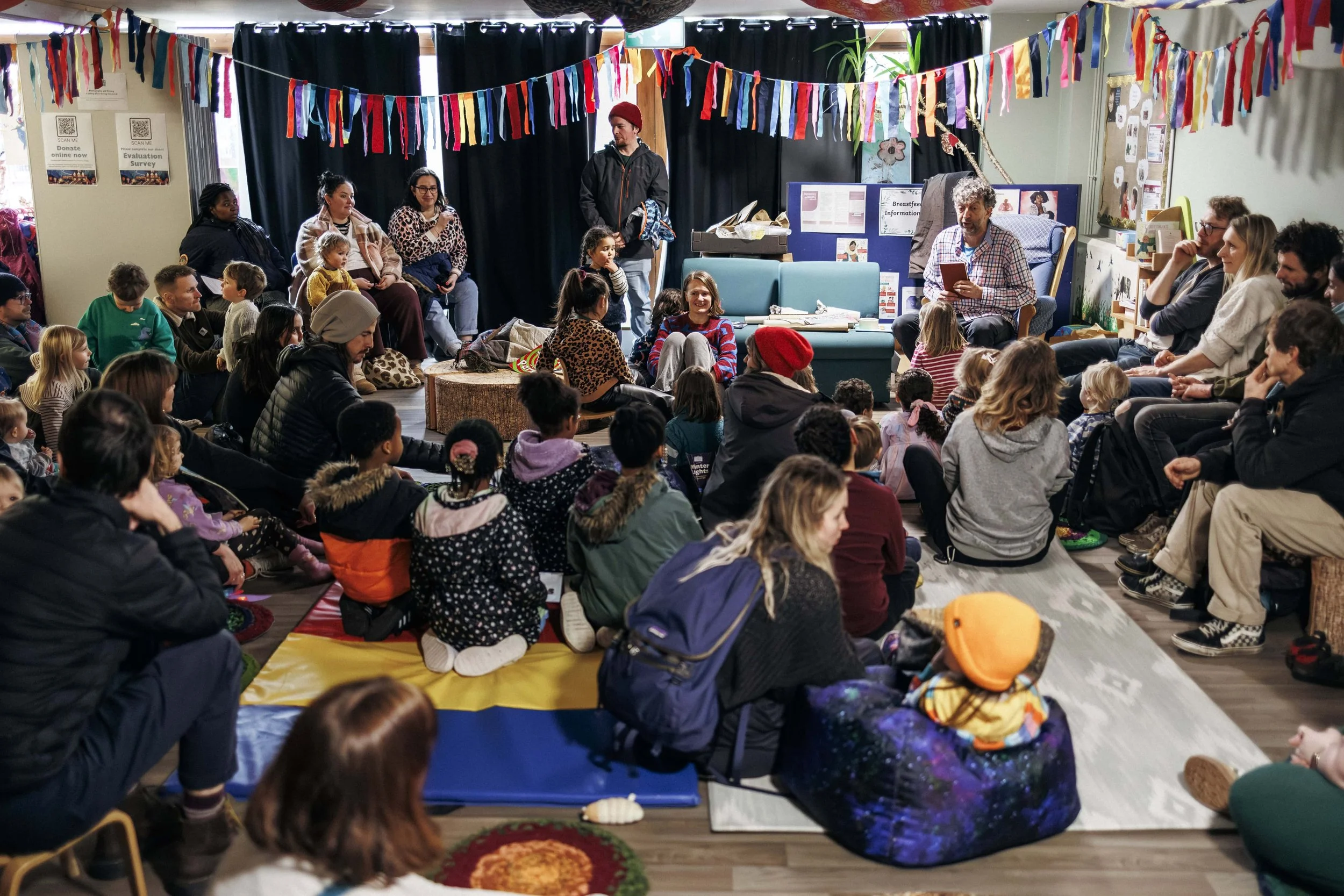 Children and adults gathered in a room for storytelling during our Winter Lights event, with colourful banners hanging overhead.
