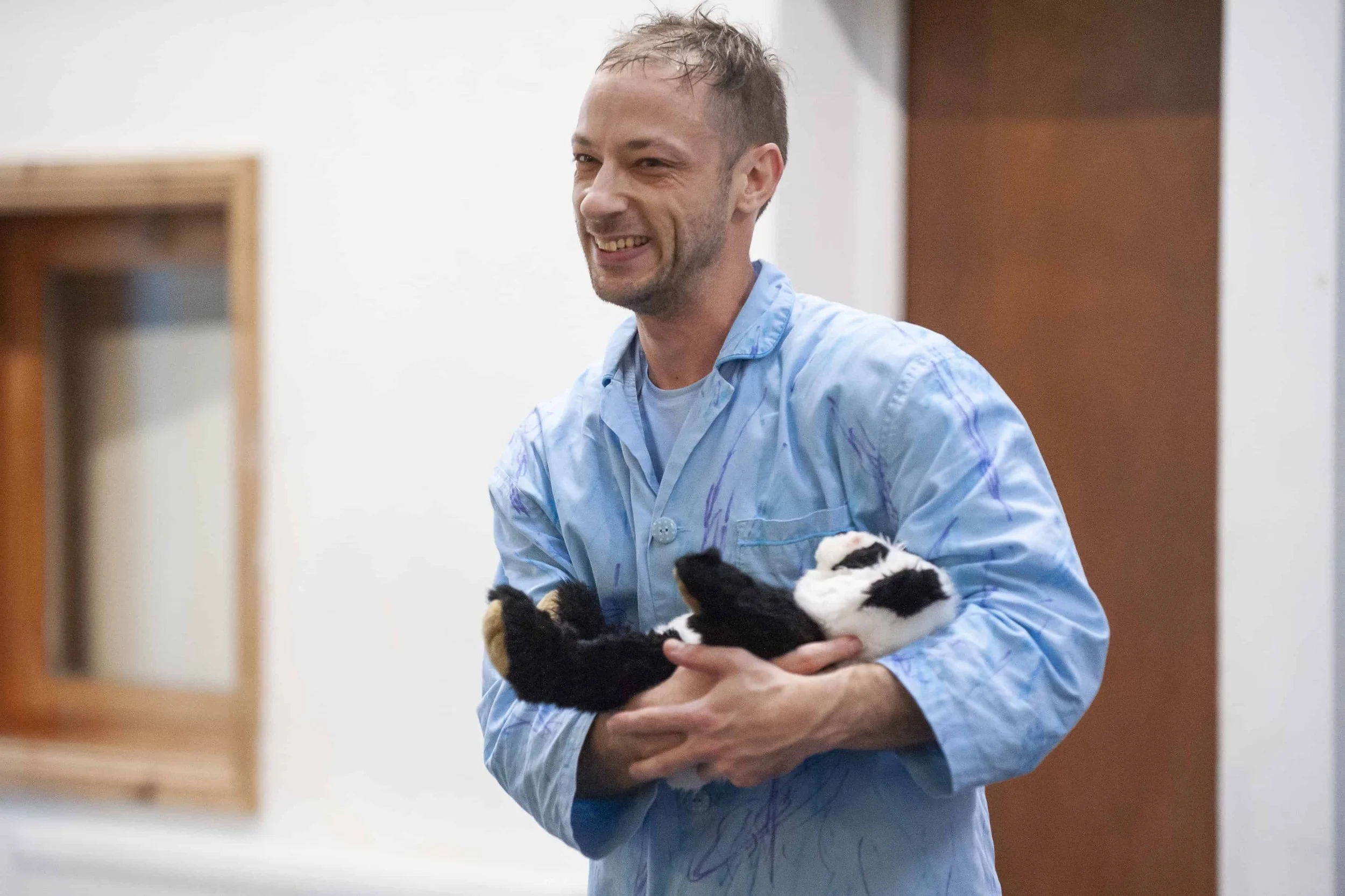 Wilkie holds a panda teddy in his arms rocking it like a baby and smiling.