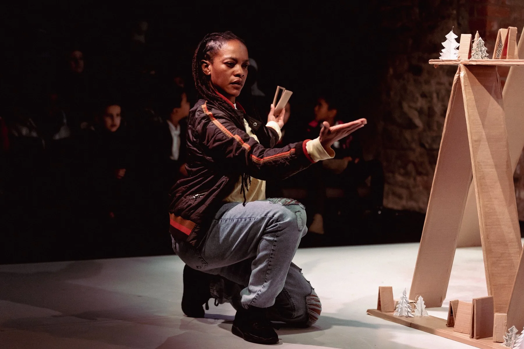 Mogali Masuku playing Sebastien in Belle and Sebastien at Bristol Old Vic. She kneels on one leg with hand palm outstretched.