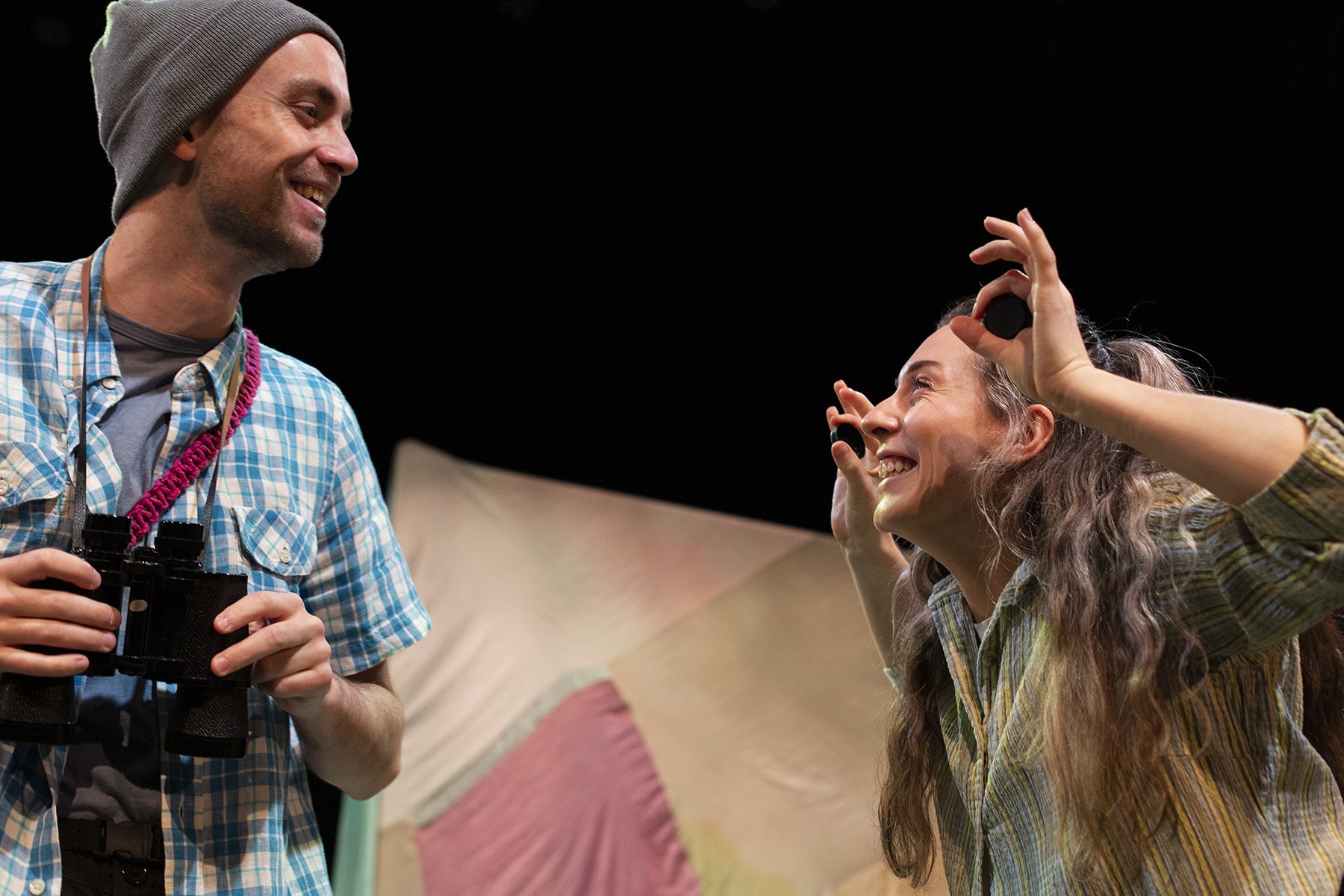 Two people smiling and holding binoculars and cameras during When The Birds Sang.