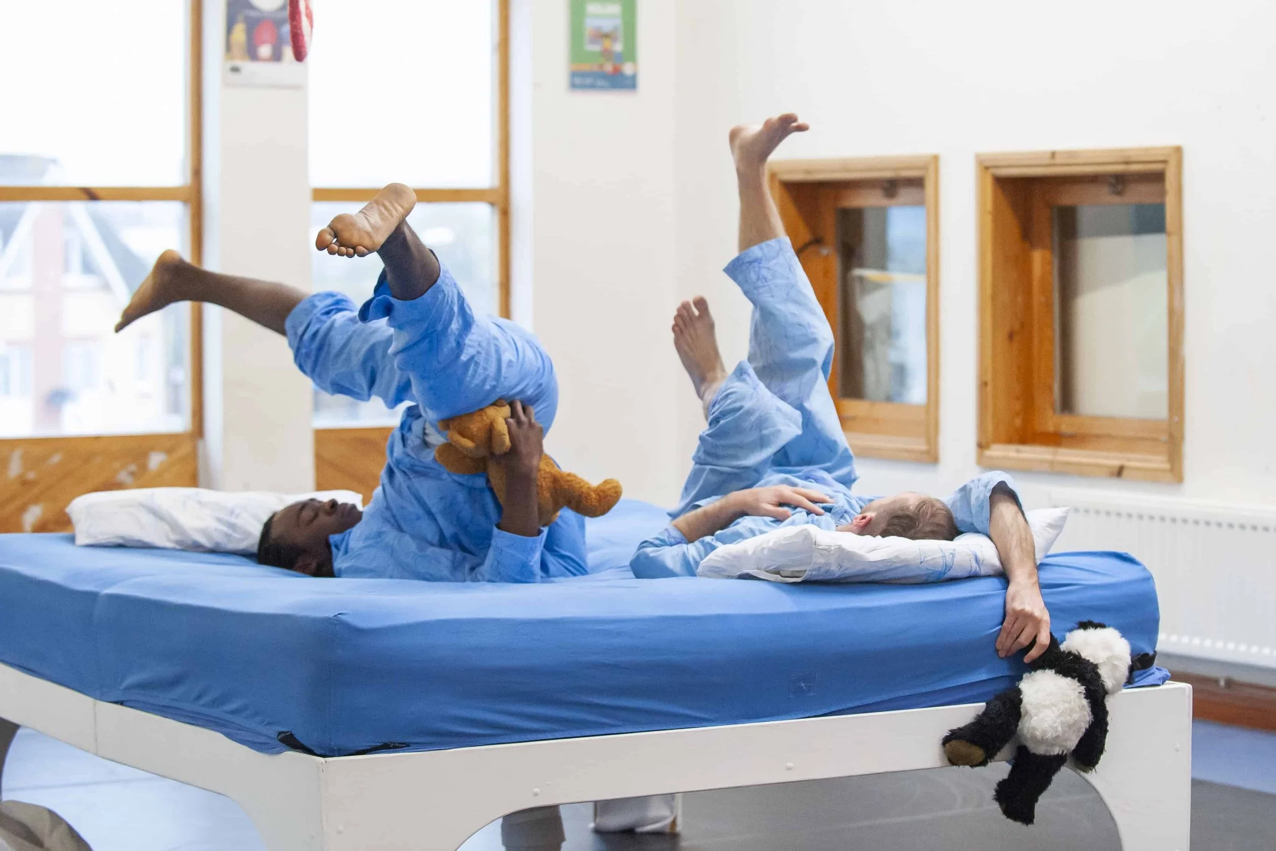Wilkie and Kel are upside down with legs in the air on a bed on a blue mattress.
