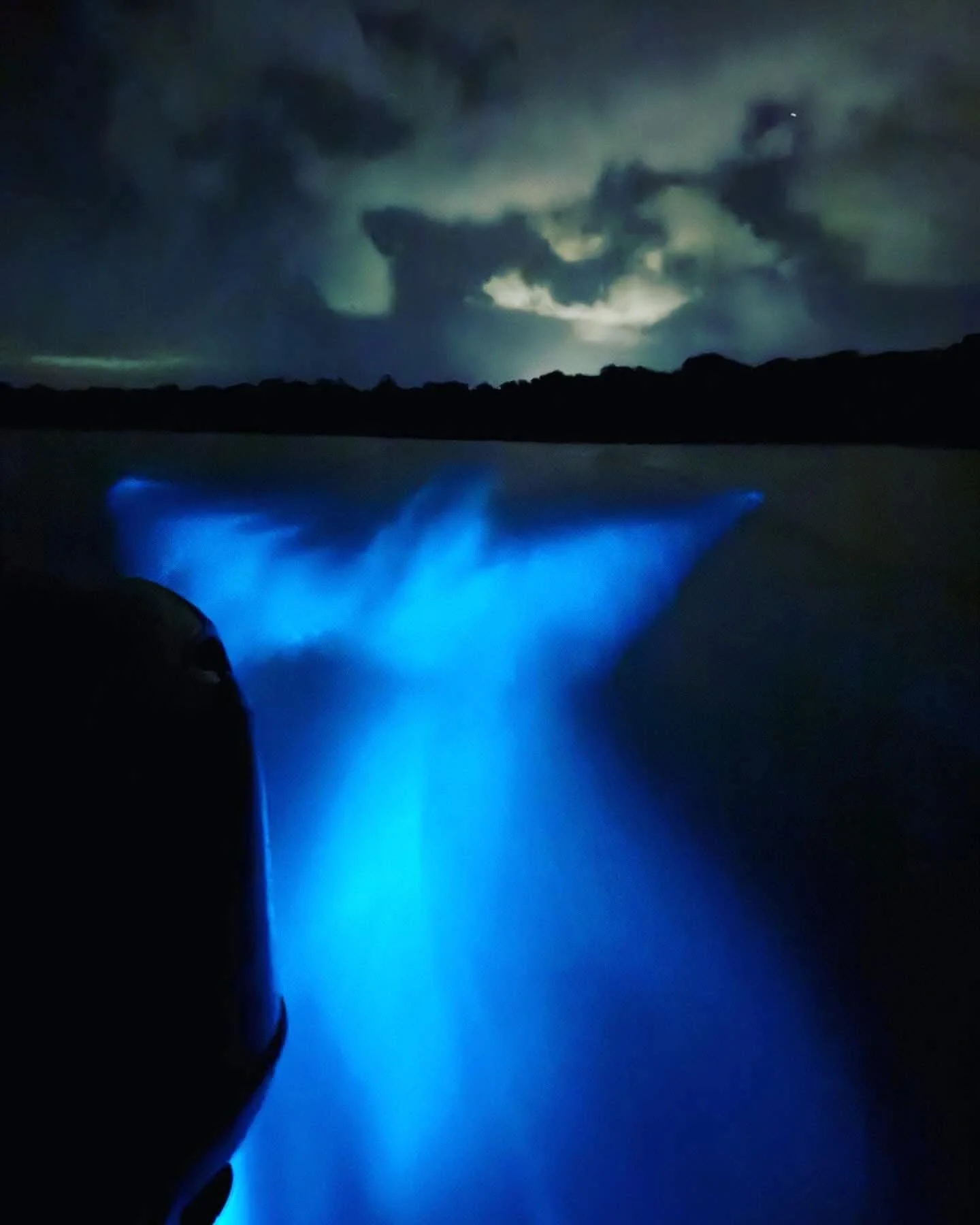 Nighttime scene of Niagara Falls illuminated with blue lights, with clouds and lightning in the dark sky.