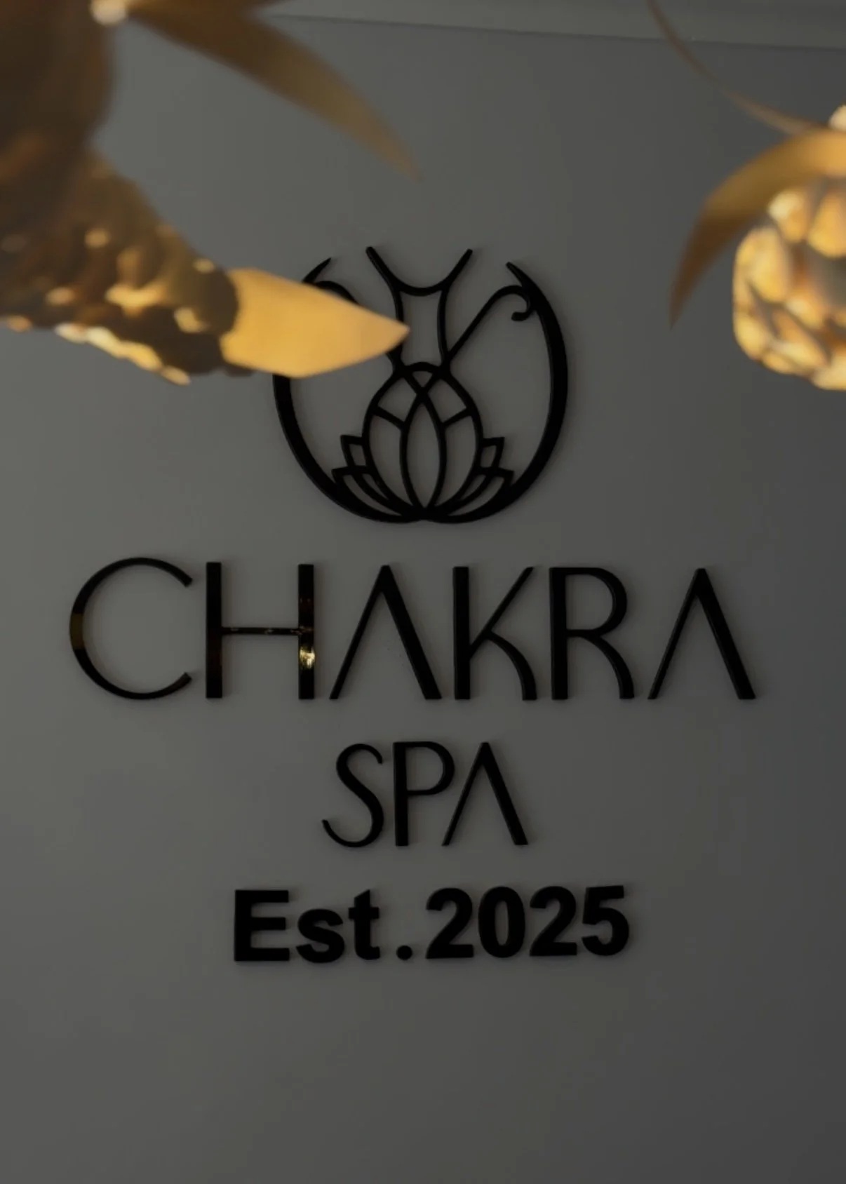 Sign for Chakra Spa with logo of a stylized lotus flower and establishment year 2025, decorated with hanging pendant lights.