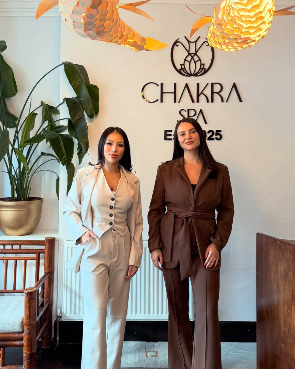 Two women standing inside a spa named Chakra Spa, with a large green plant beside them and hanging paper lanterns on the ceiling. Maria and Sandra are the owners.